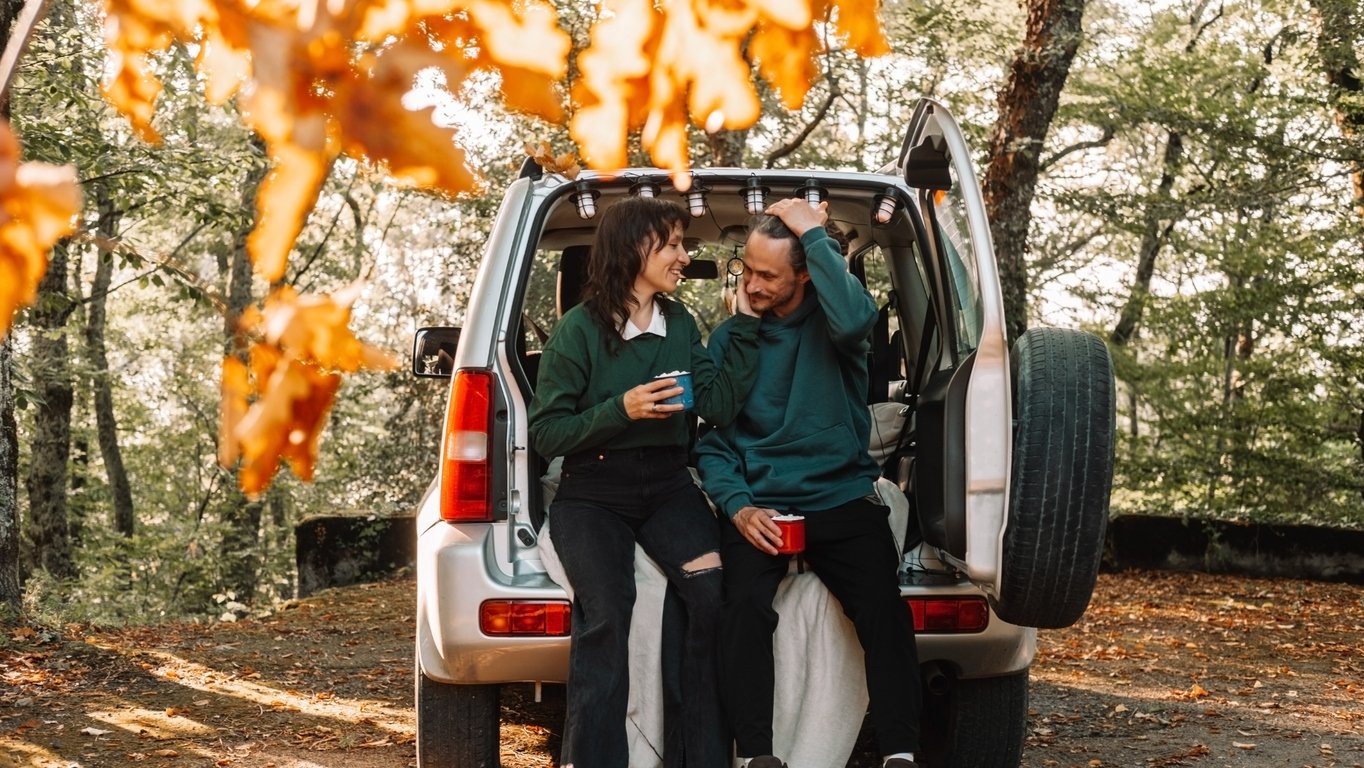 A man and a woman are sitting in the trunk of a car in the woods and talking to each other