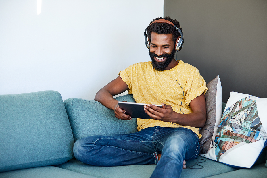 man with headphones on sofa looking at tablet