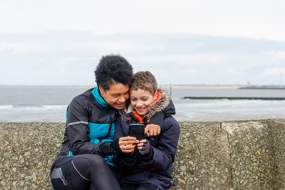 mother and child looking at phone next to sea