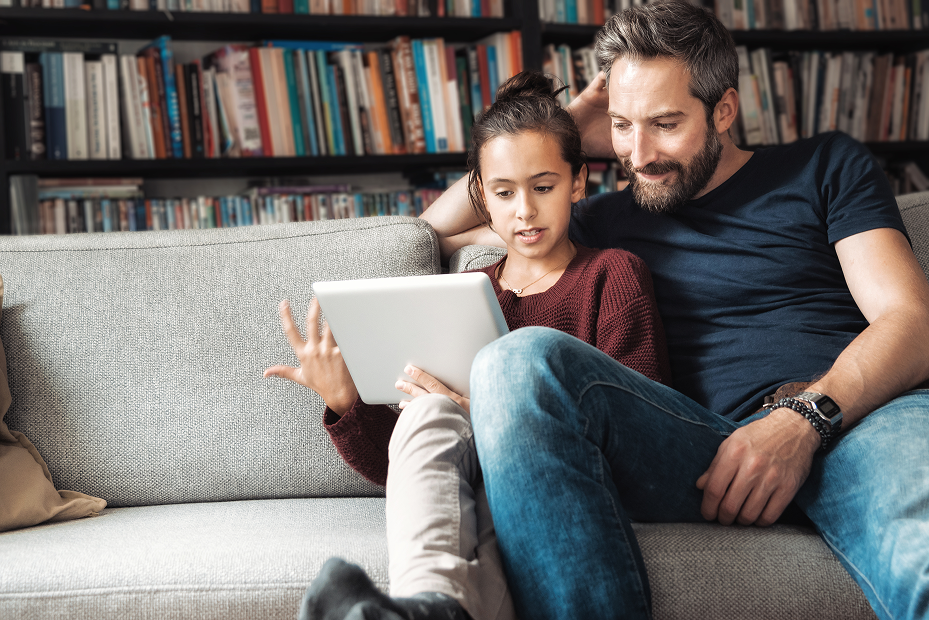 man and child sitting on the sofa with a ipad in the child's hand