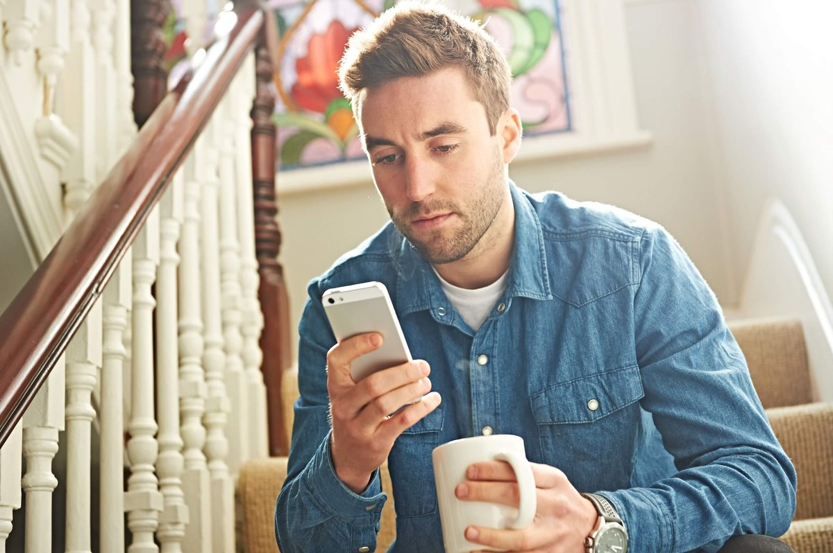 man sitting on stair with phone and cup of tea in hand