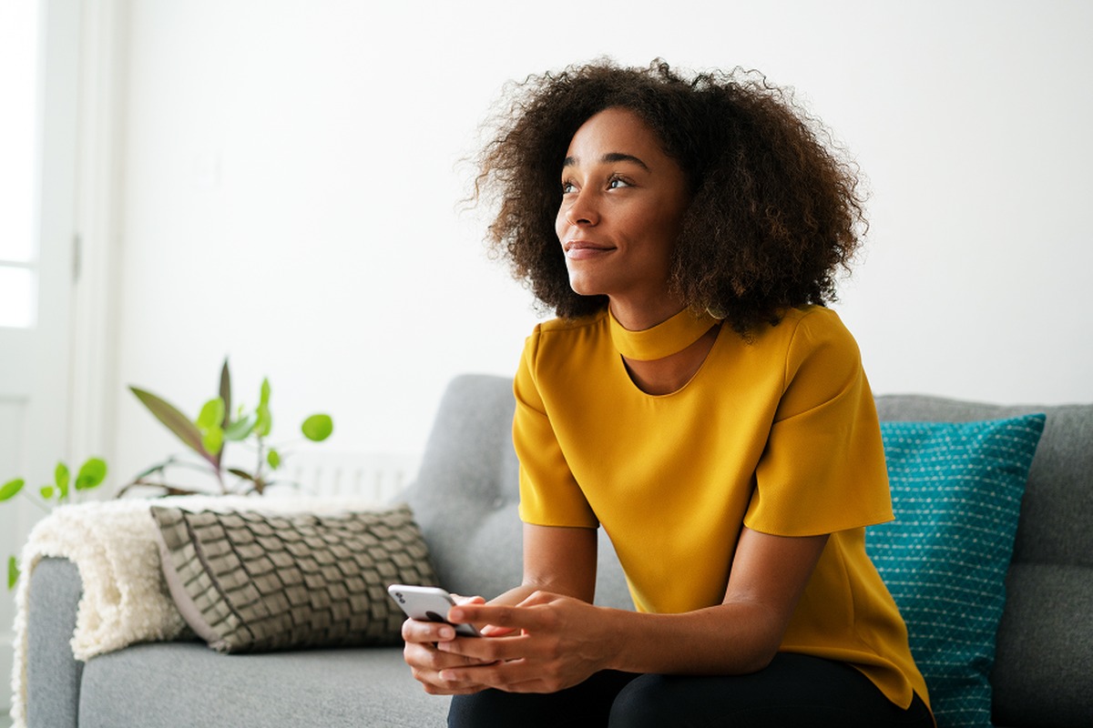 woman in yellow top looking into the distance with phone in her hand
