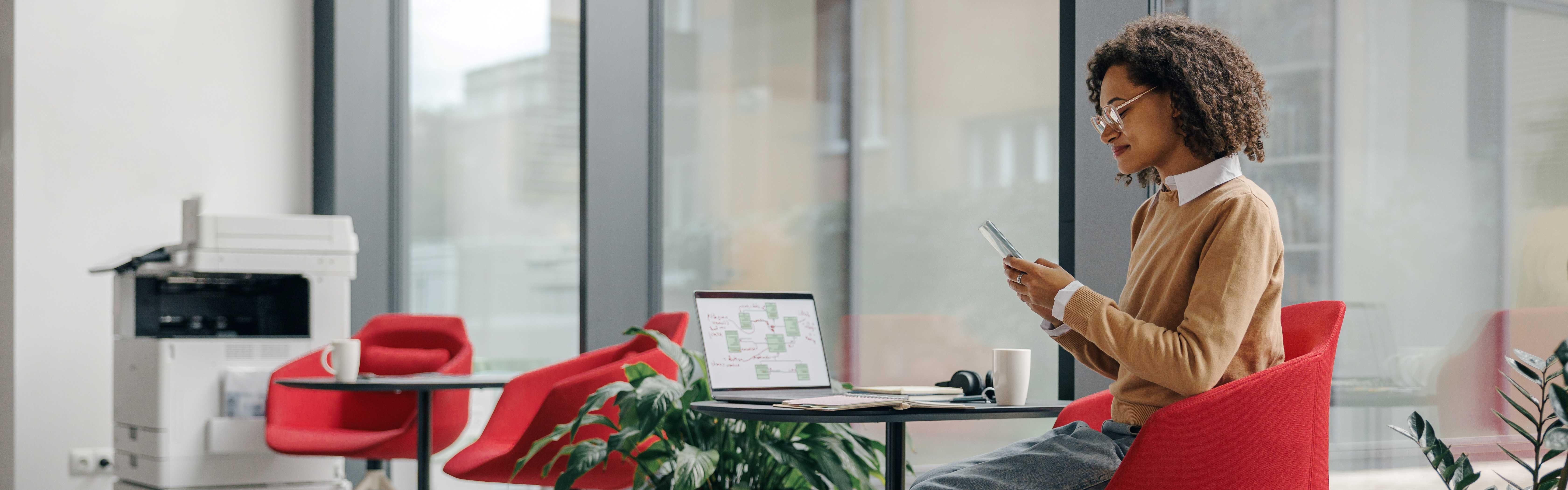 Female manager is use phone while working on laptop in modern office near window