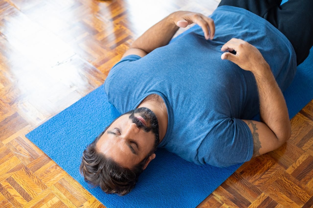 Man lying on a blue yoga mat stretching his back with eyes closed