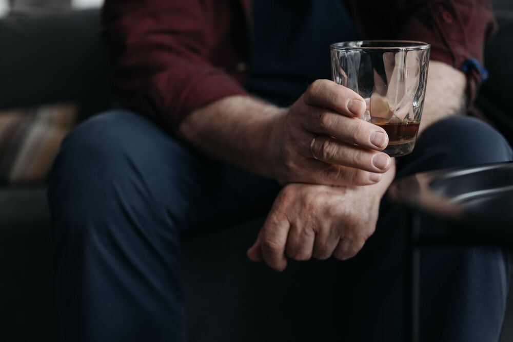 Close-up of a man's hand holding a glass of whisky while seated