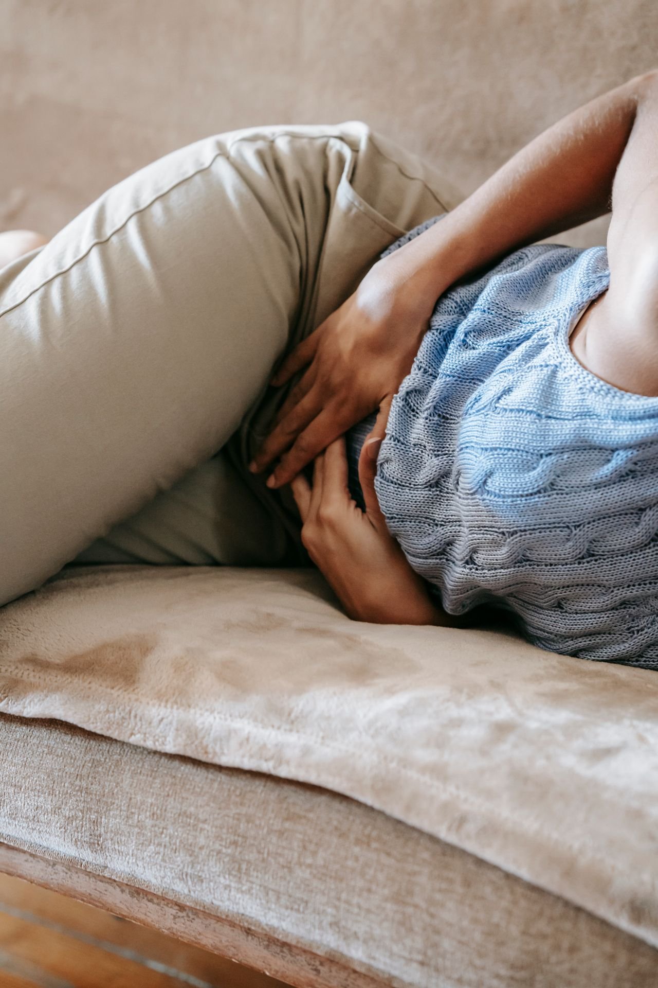 Woman sitting on a sofa holding her stomach in discomfort