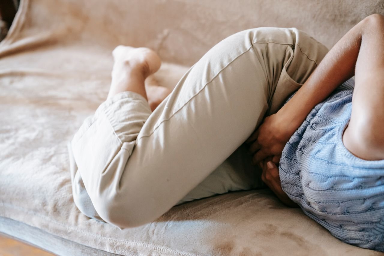 Woman sitting on a sofa holding her stomach in discomfort