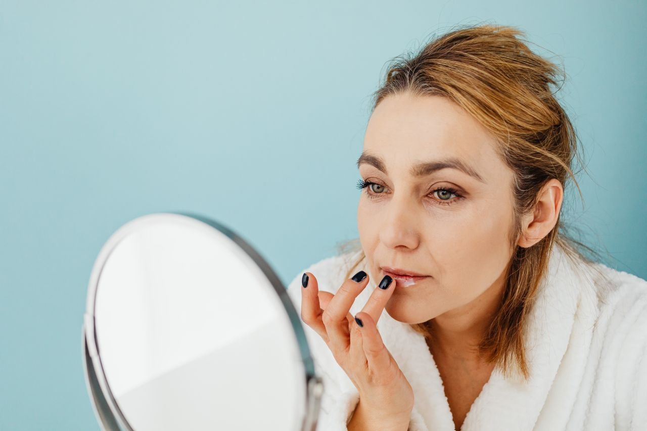 Woman applying lip balm while looking in a hand mirror