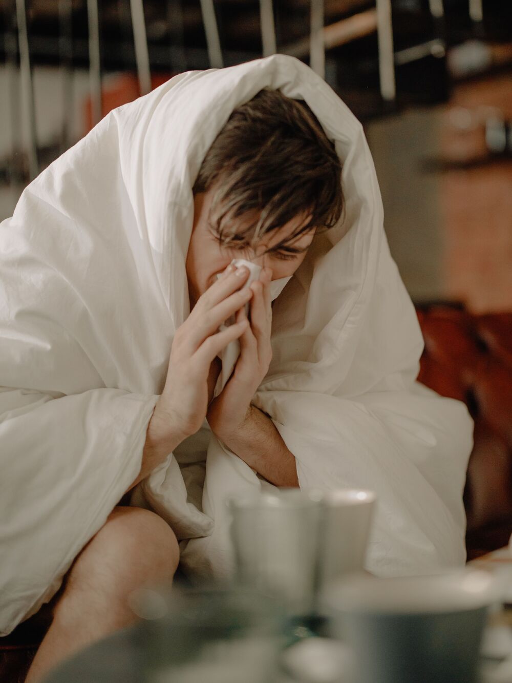 man blowing nose under duvet