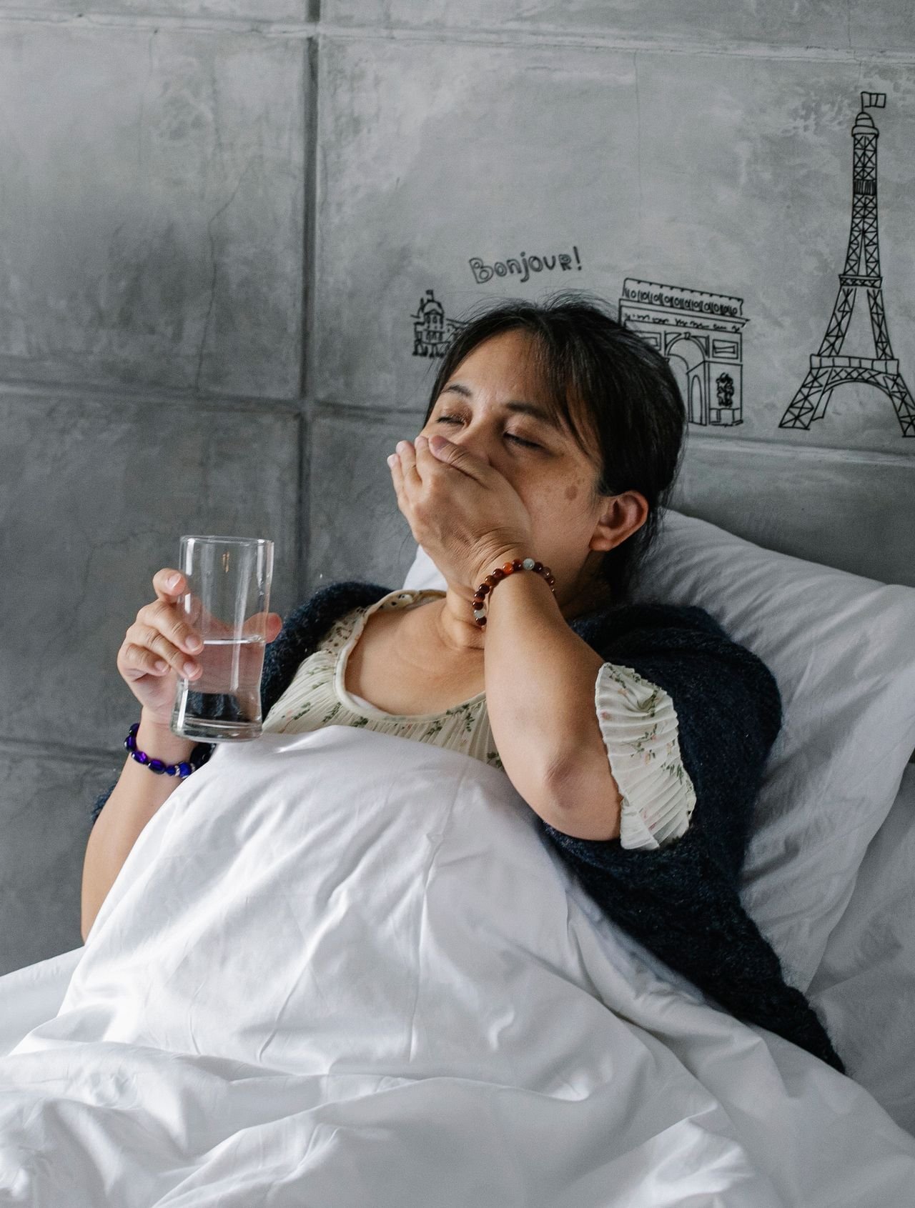 Woman lying in bed holding a glass of water while taking medication