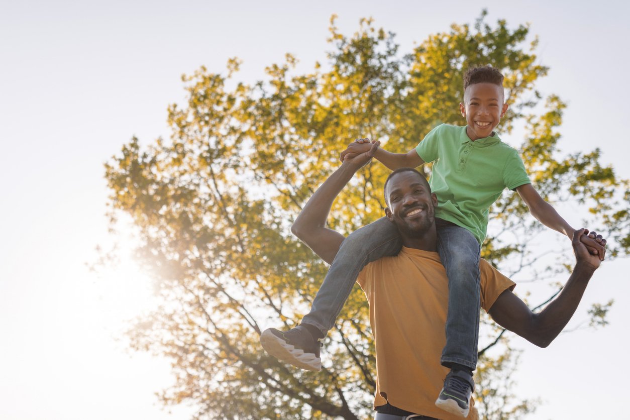 Elementary age boy having fun with his father outdoors, sitting on his shoulders