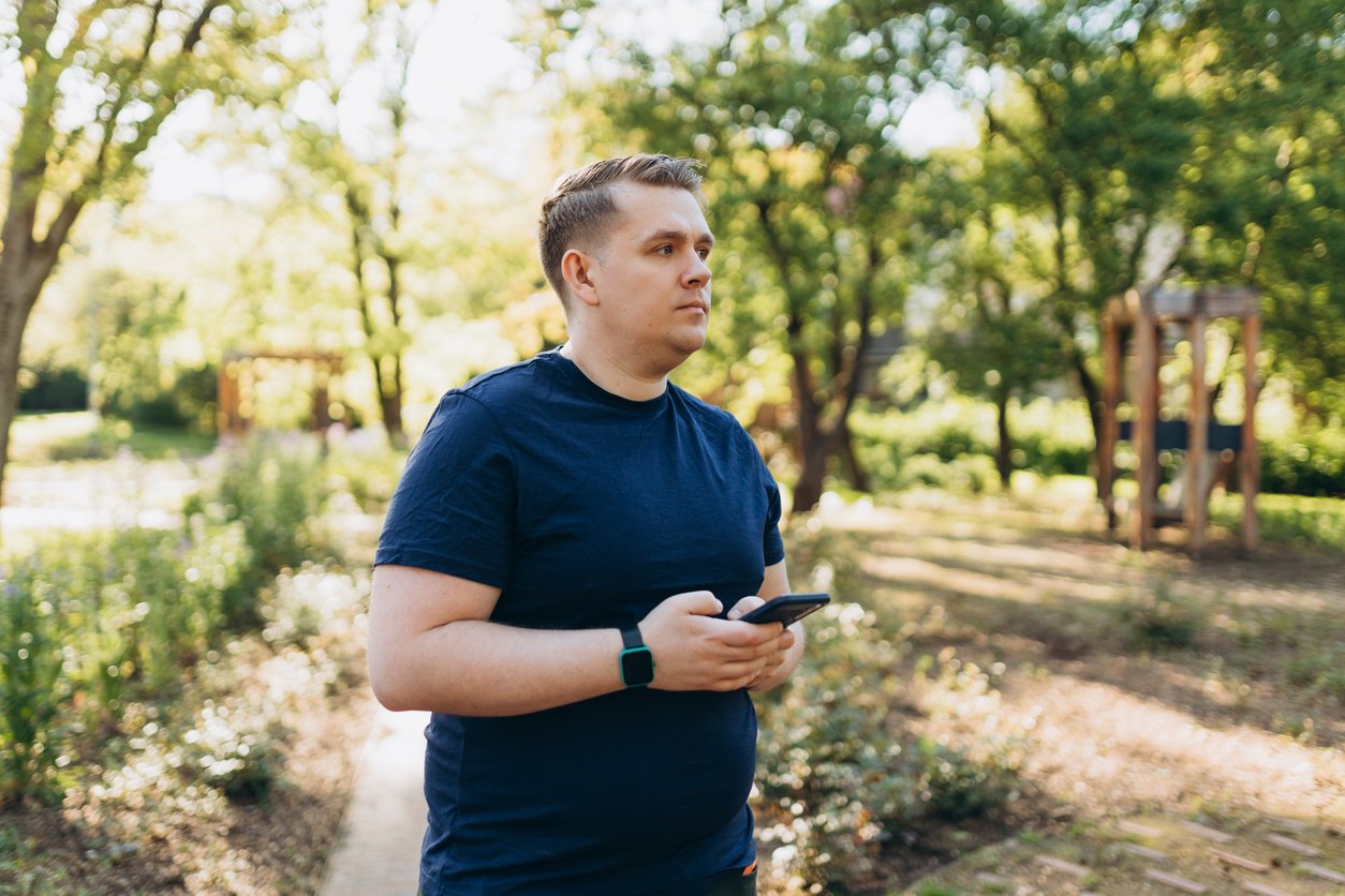 A man standing outdoors on a path surrounded by greenery, looking at his phone.