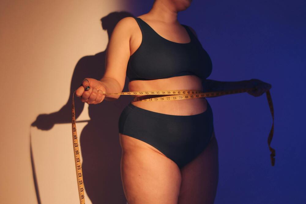Woman measuring her waist with a tape measure against a dramatic blue and orange lit background
