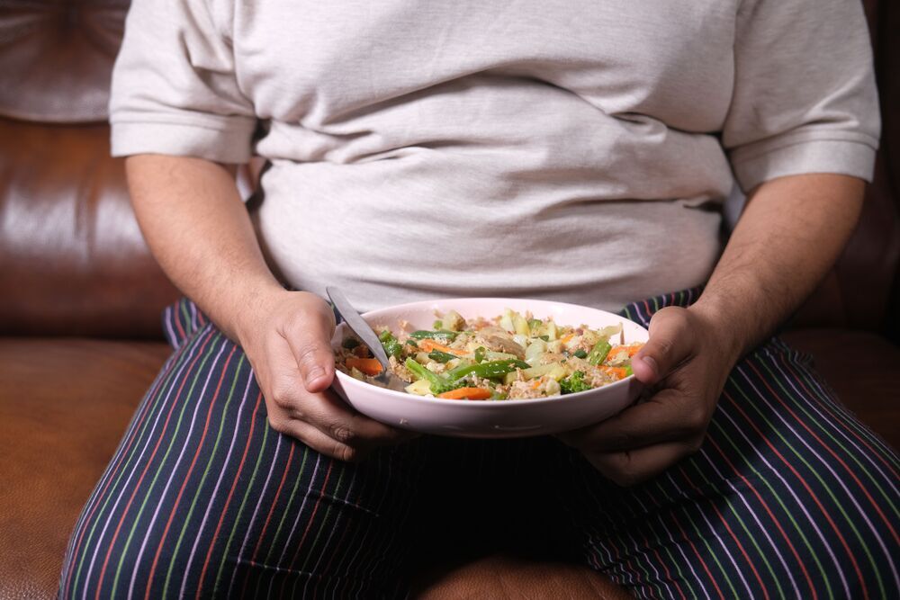 Man sitting on a sofa holding a bowl of vegetable stir-fry on his lap