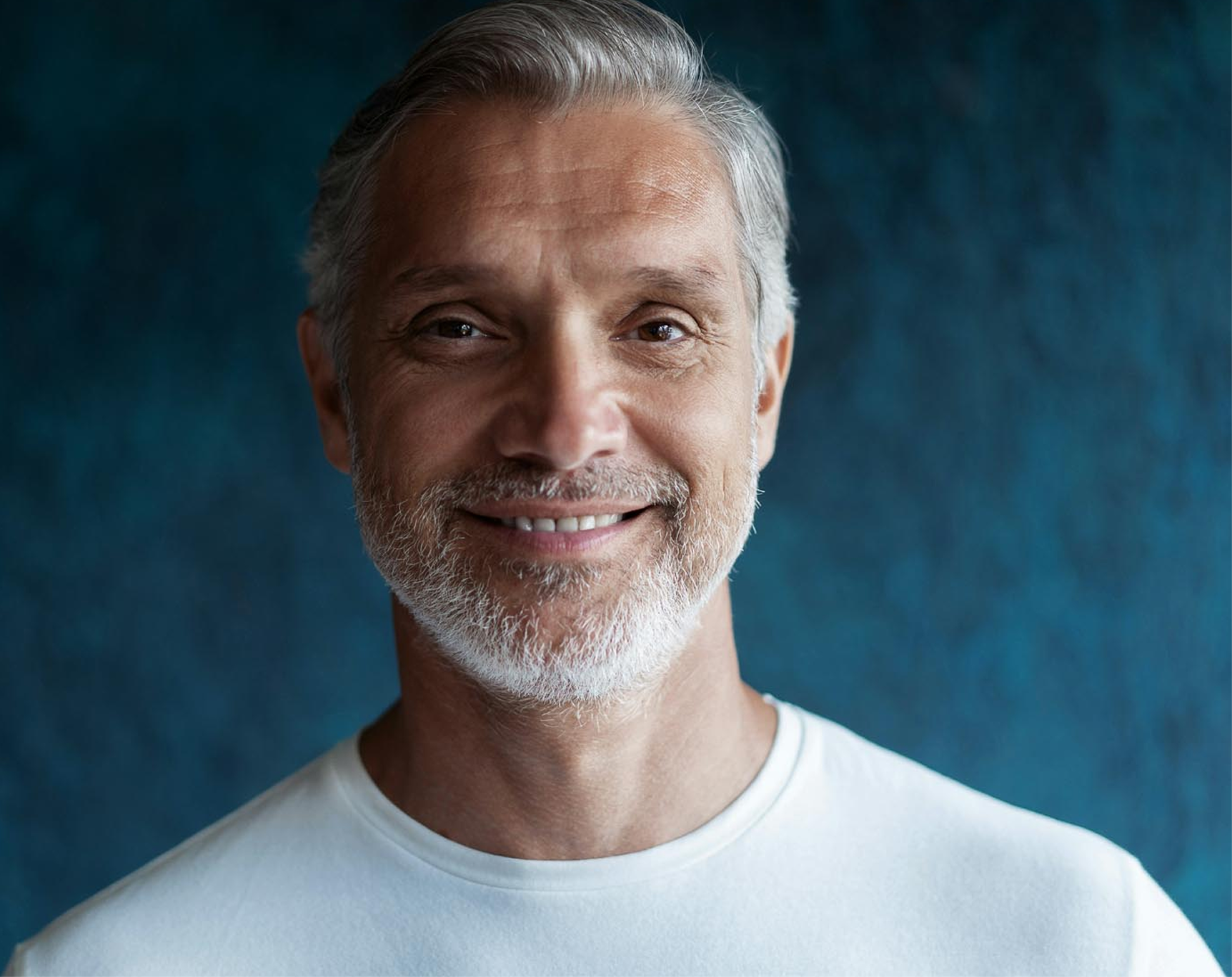 Man wearing a white tshirt and white hair standing behind a dark blue background