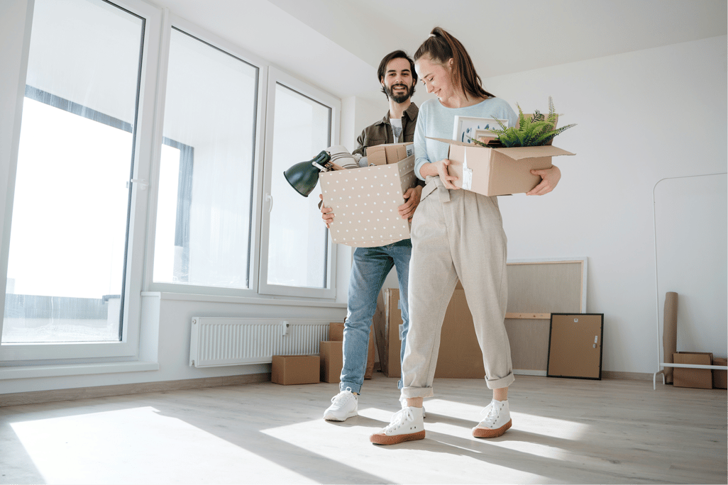 Man and woman in a living room holding boxes and surrounded by boxes