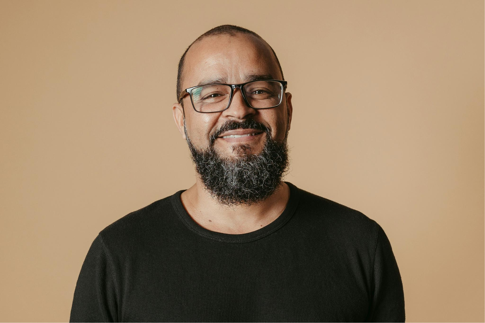 Man with glasses and beard standing behind a cream background