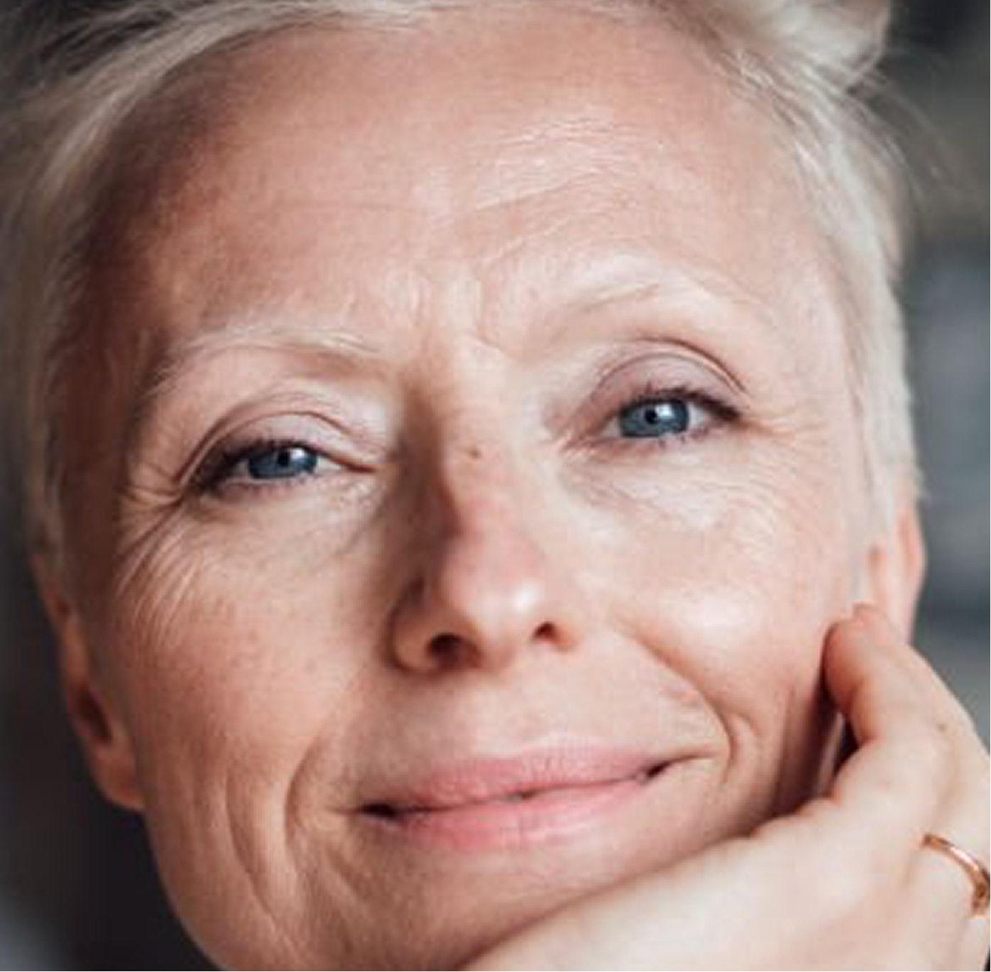 Close-up portrait of an older woman with short grey hair smiling gently with her hand resting on her chin