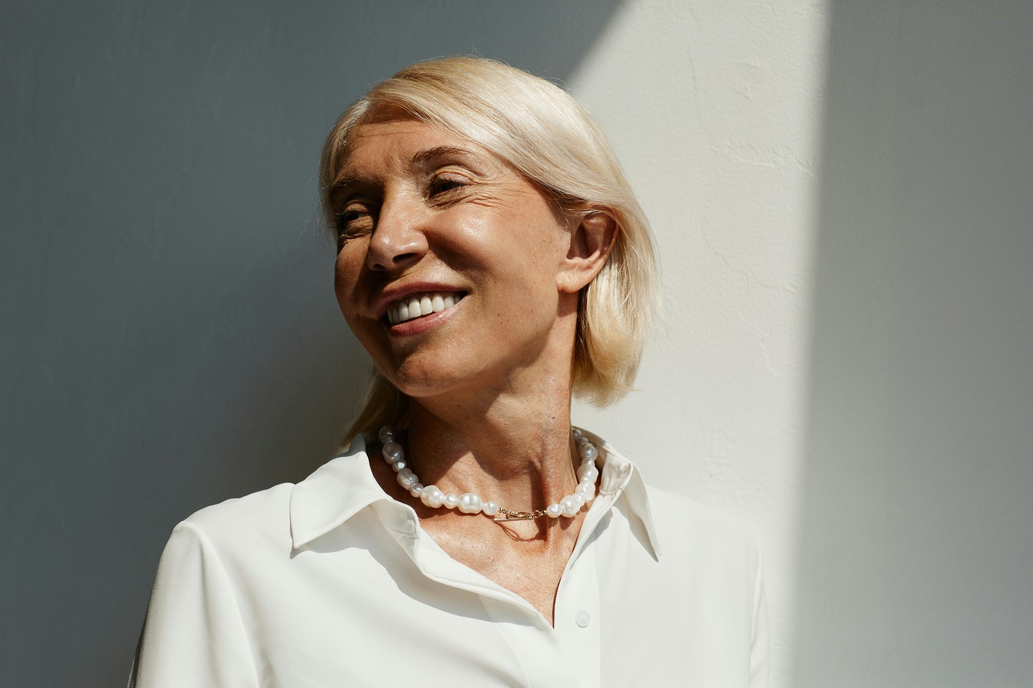 Smiling older woman with blonde hair and a pearl necklace looking to the side in sunlight