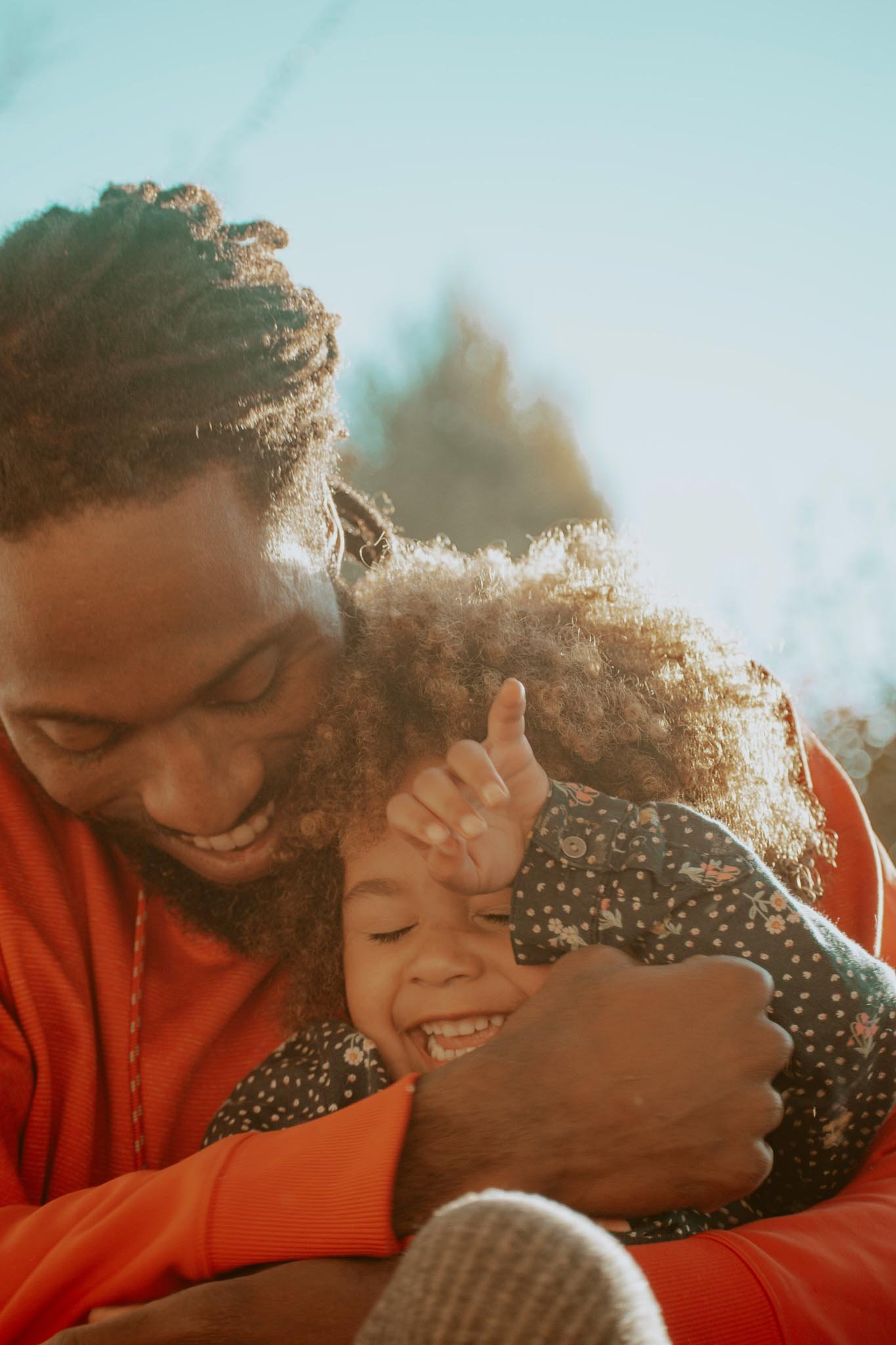 Close-up of a bearded man affectionately holding his young daughter in sunlight