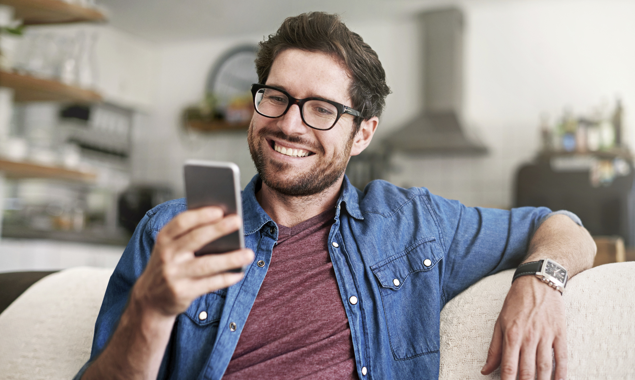Smiling man holding his phone while relaxing on a sofa, next to text reading 