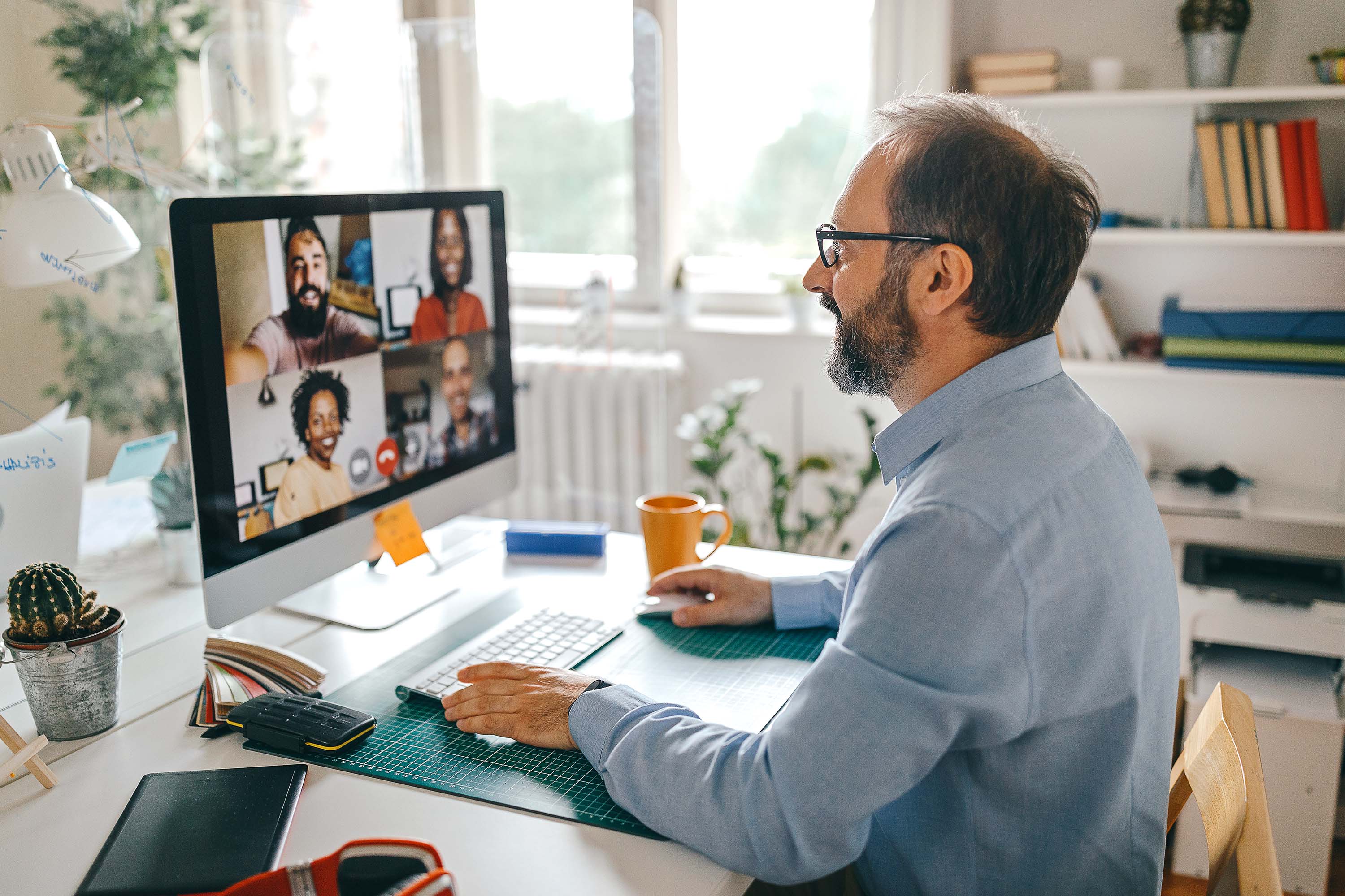 Man on a video call with four colleagues on his desktop monitor, holding a mug