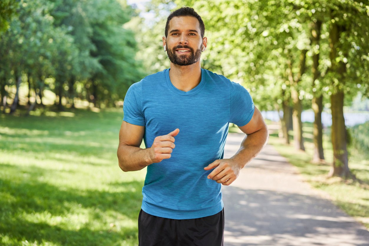 Smiling man running in park at sunny summer day