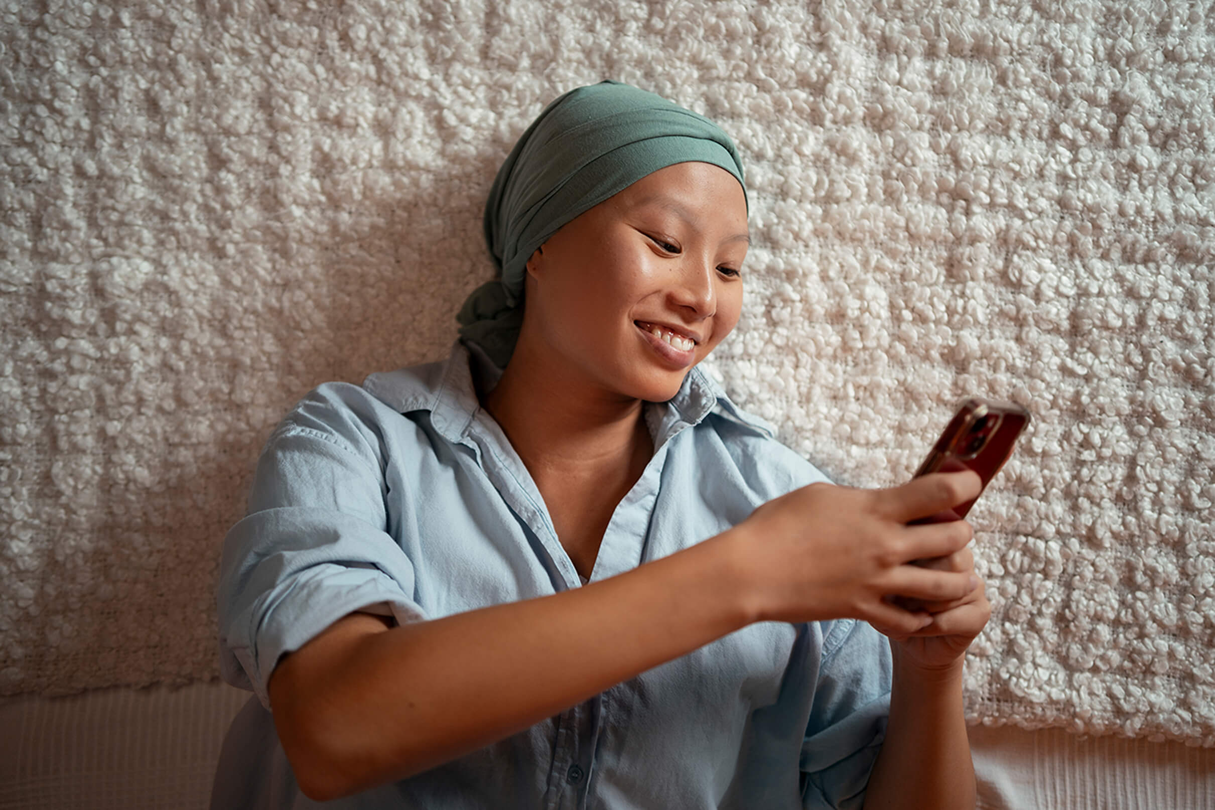 Female presenting person smiling at phone with headcover on