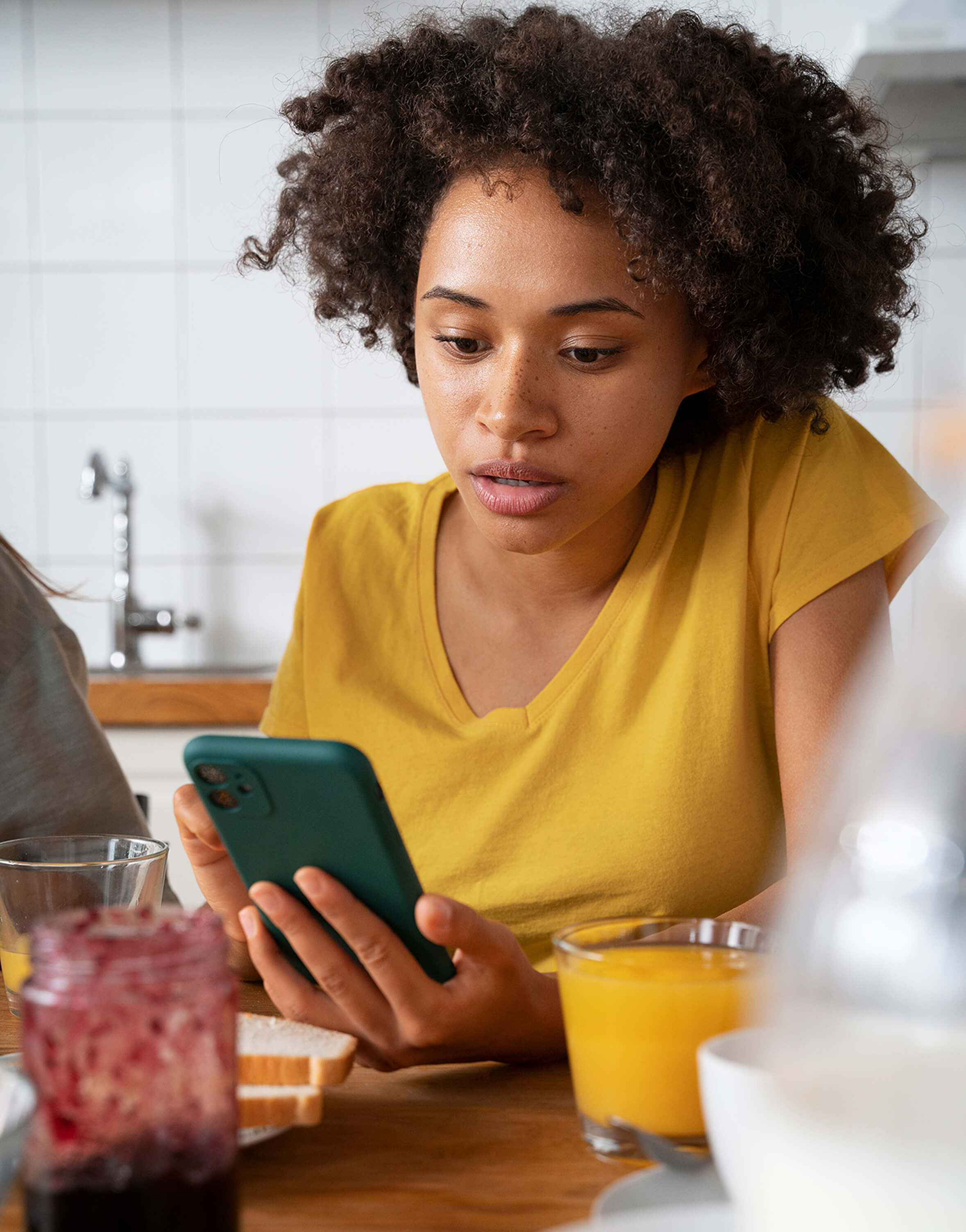 Female presenting person using phone at desk with orange juice