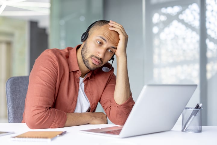 Sad bored man with headset working inside office with laptop,