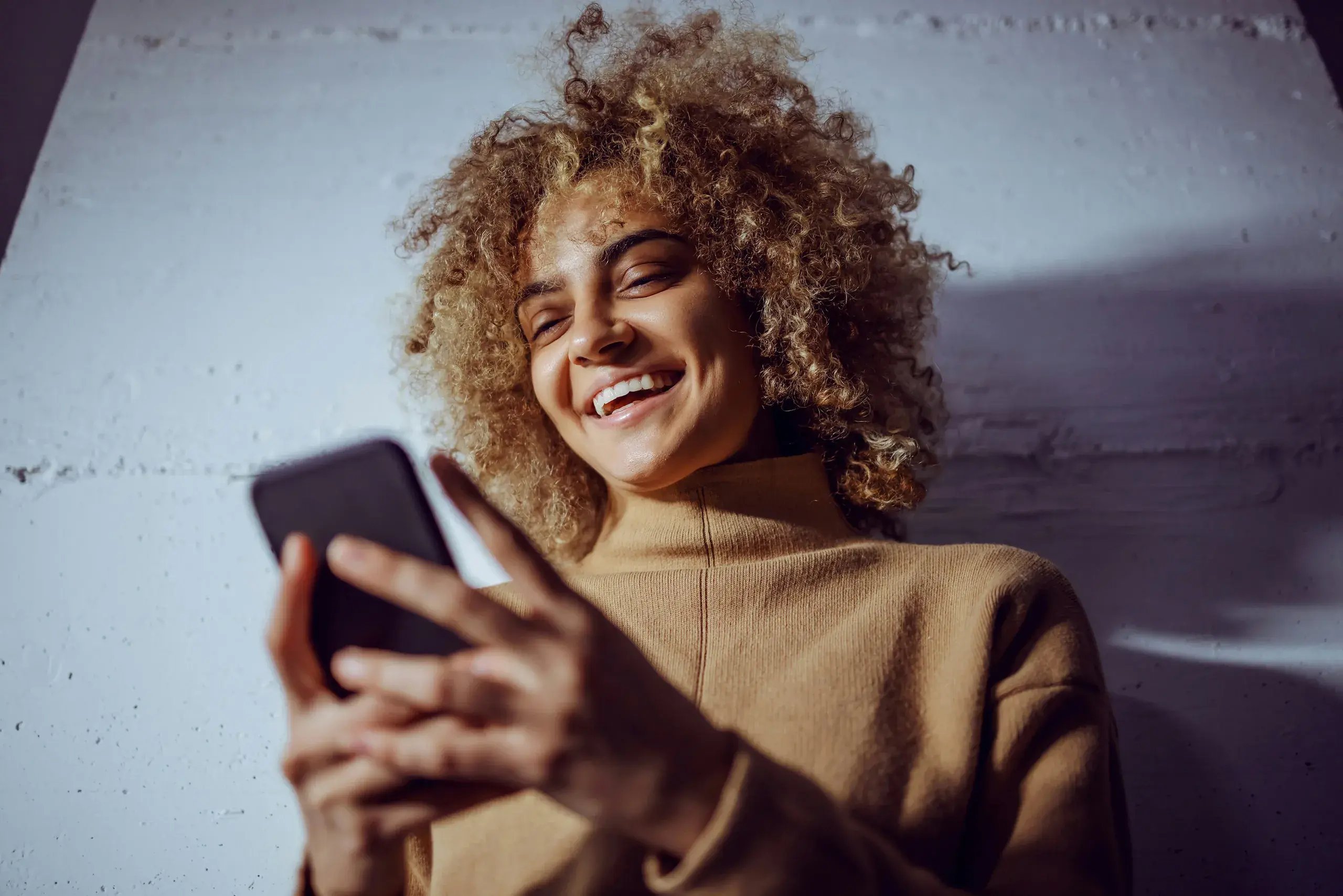 Close-up of a smiling woman with curly hair holding her phone
