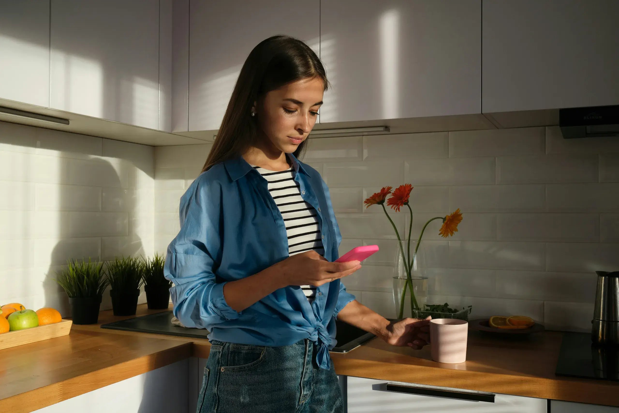 Woman checking her phone while standing in a sunlit kitchen