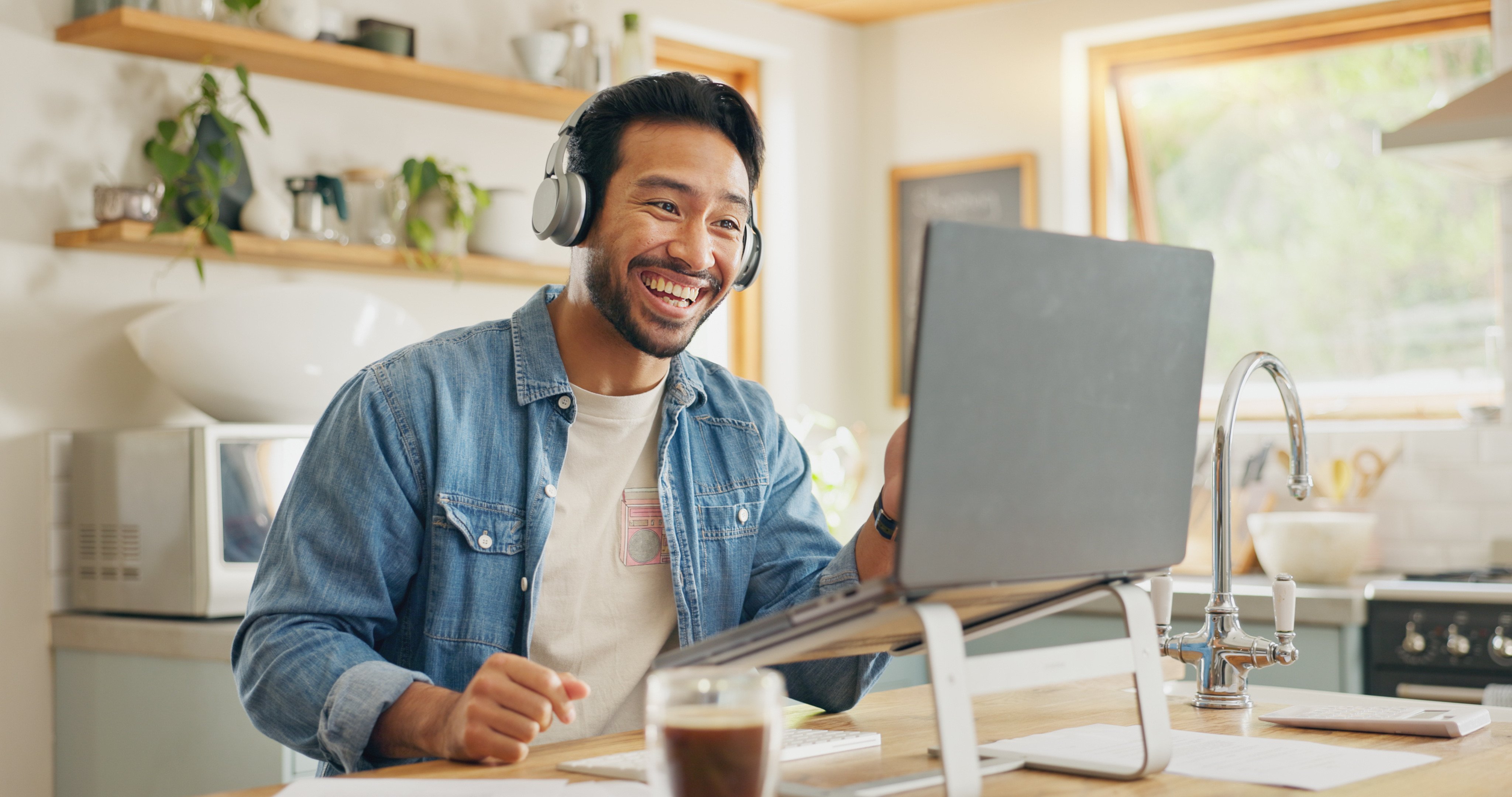 man smiling wearing headphones on laptop in kitchen