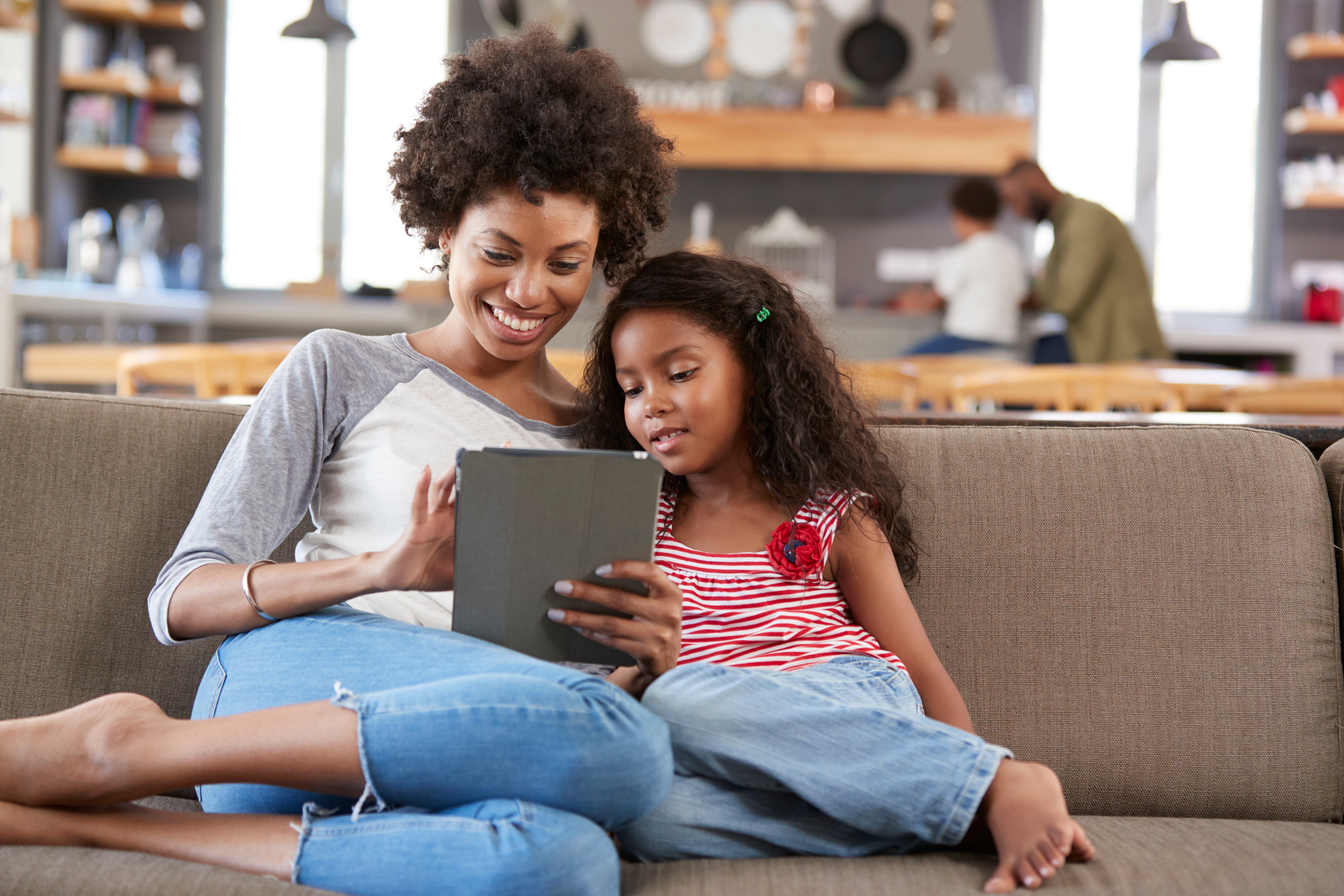 Mother and daughter looking at a tablet together on a sofa in a café
