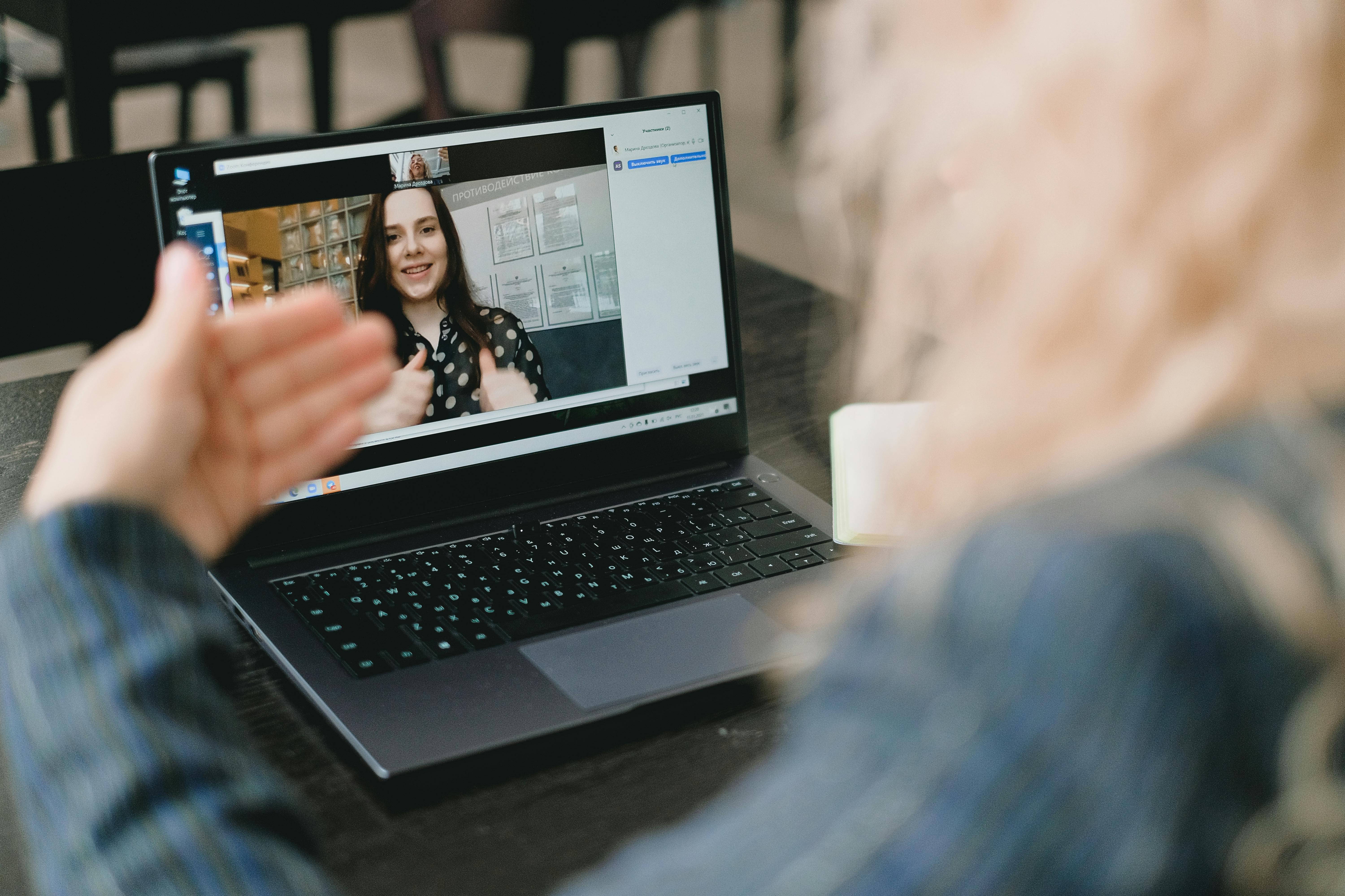 person waving during a video call with a woman on a laptop screen