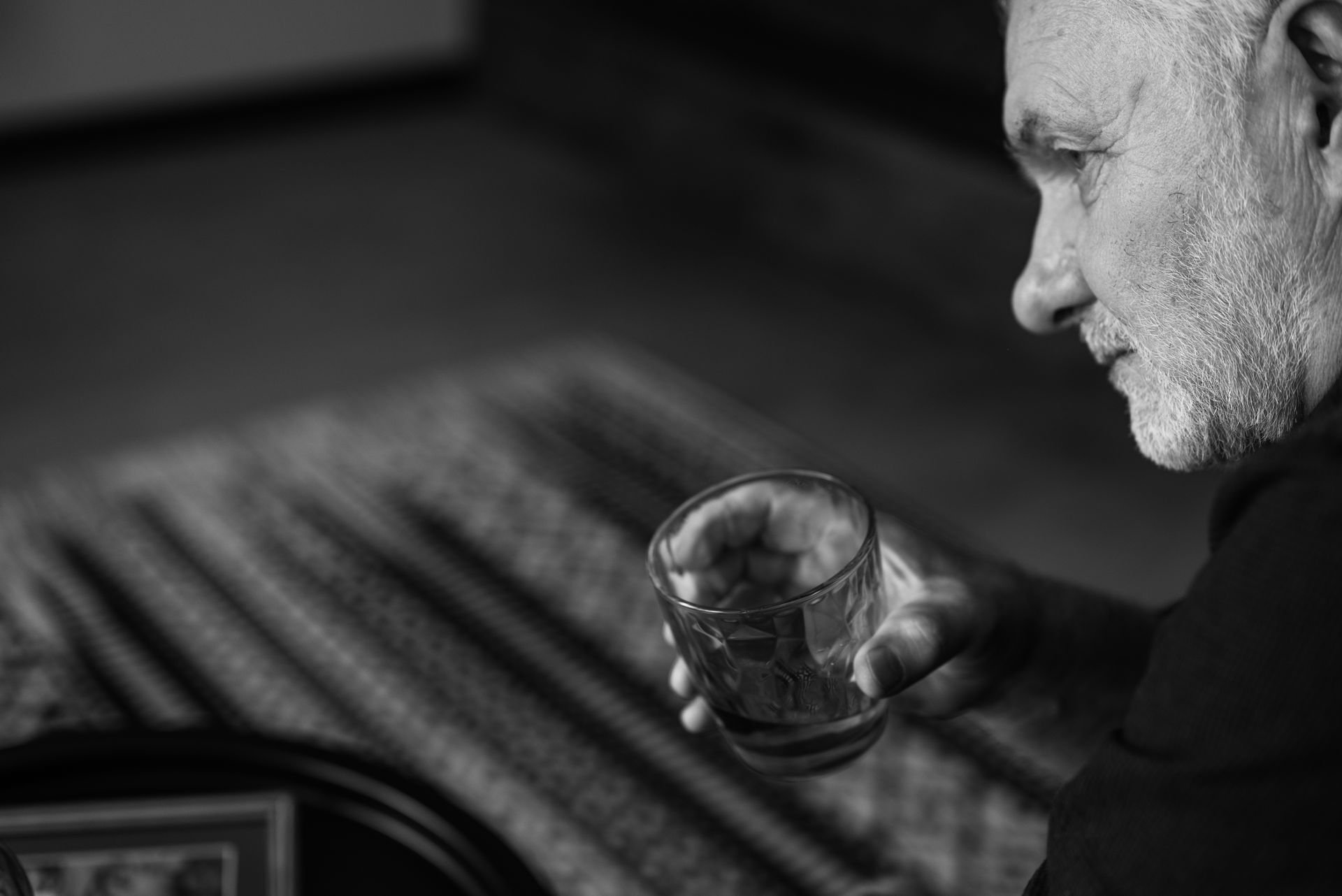 Black-and-white profile of an older bearded man gazing down at a glass of alcohol held in his hand
