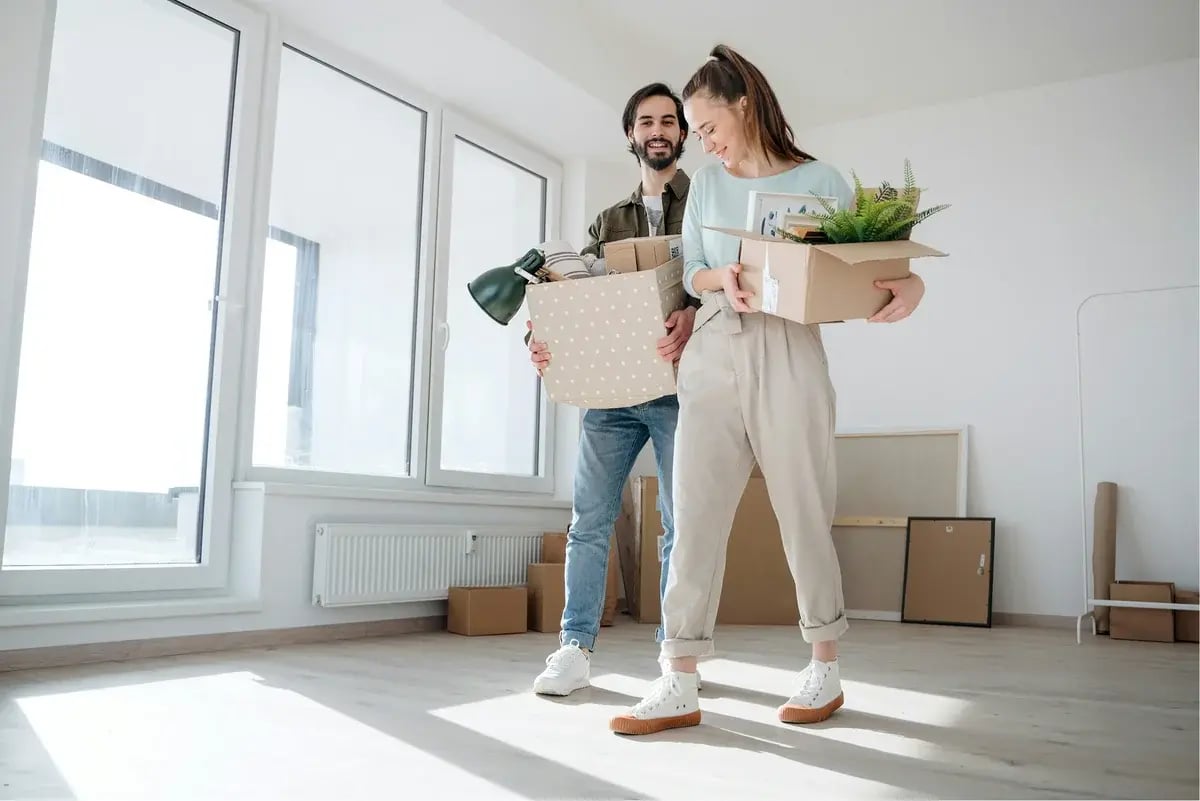 Man and woman in a living room holding boxes and surrounded by boxes