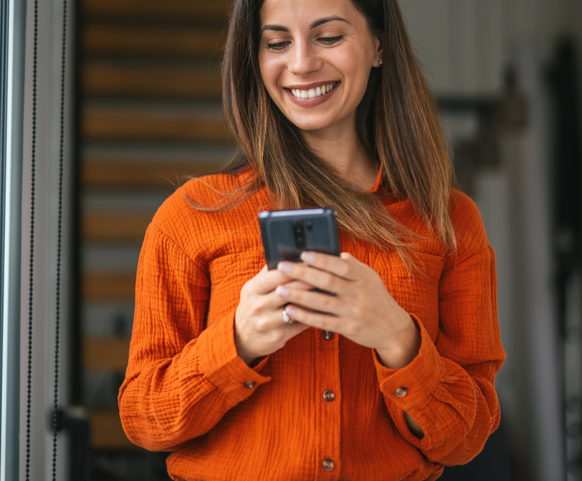 smiling woman in an orange top holding her phone
