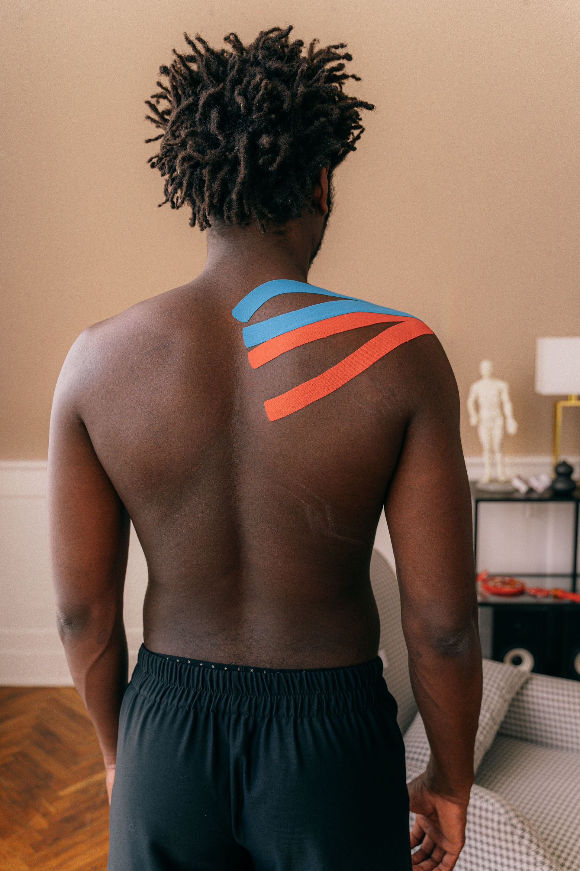 Man's bare back with blue and orange kinesiology tape applied over his shoulder