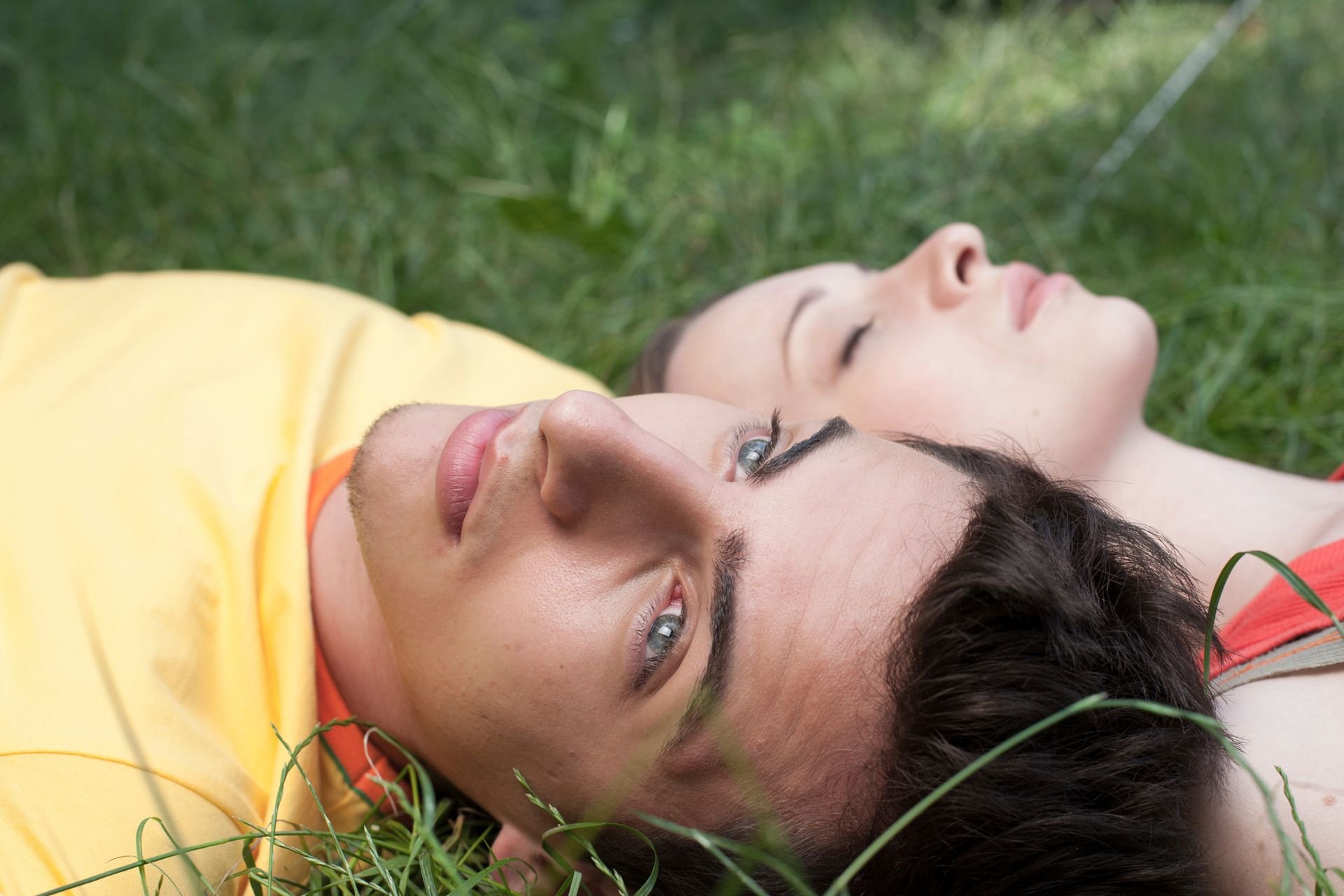 Couple lying together in the grass, foreheads touching with eyes closed