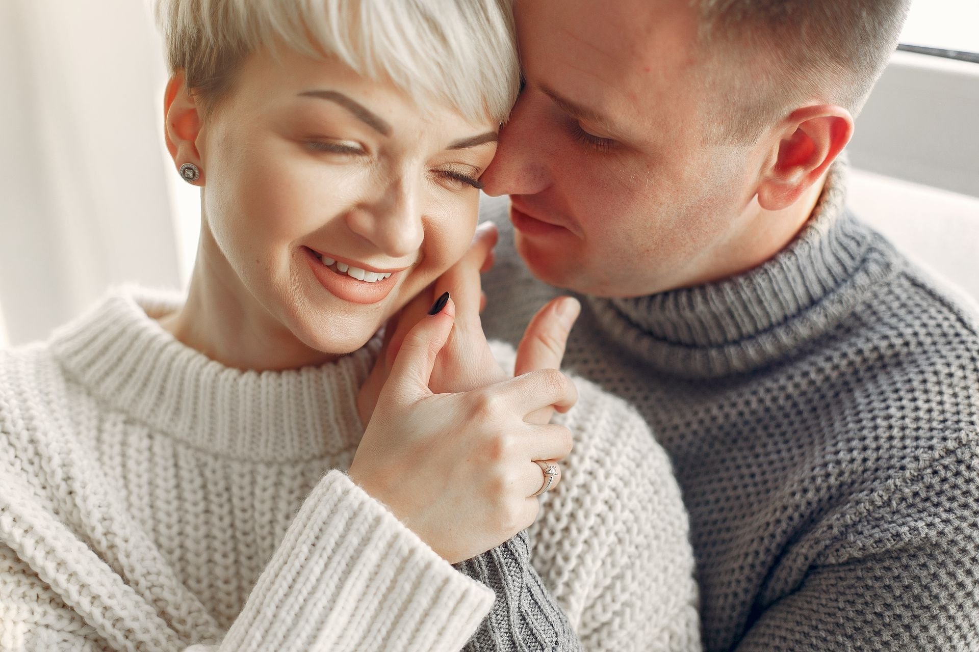 Couple embracing closely, smiling with eyes closed, wearing cosy knit jumpers