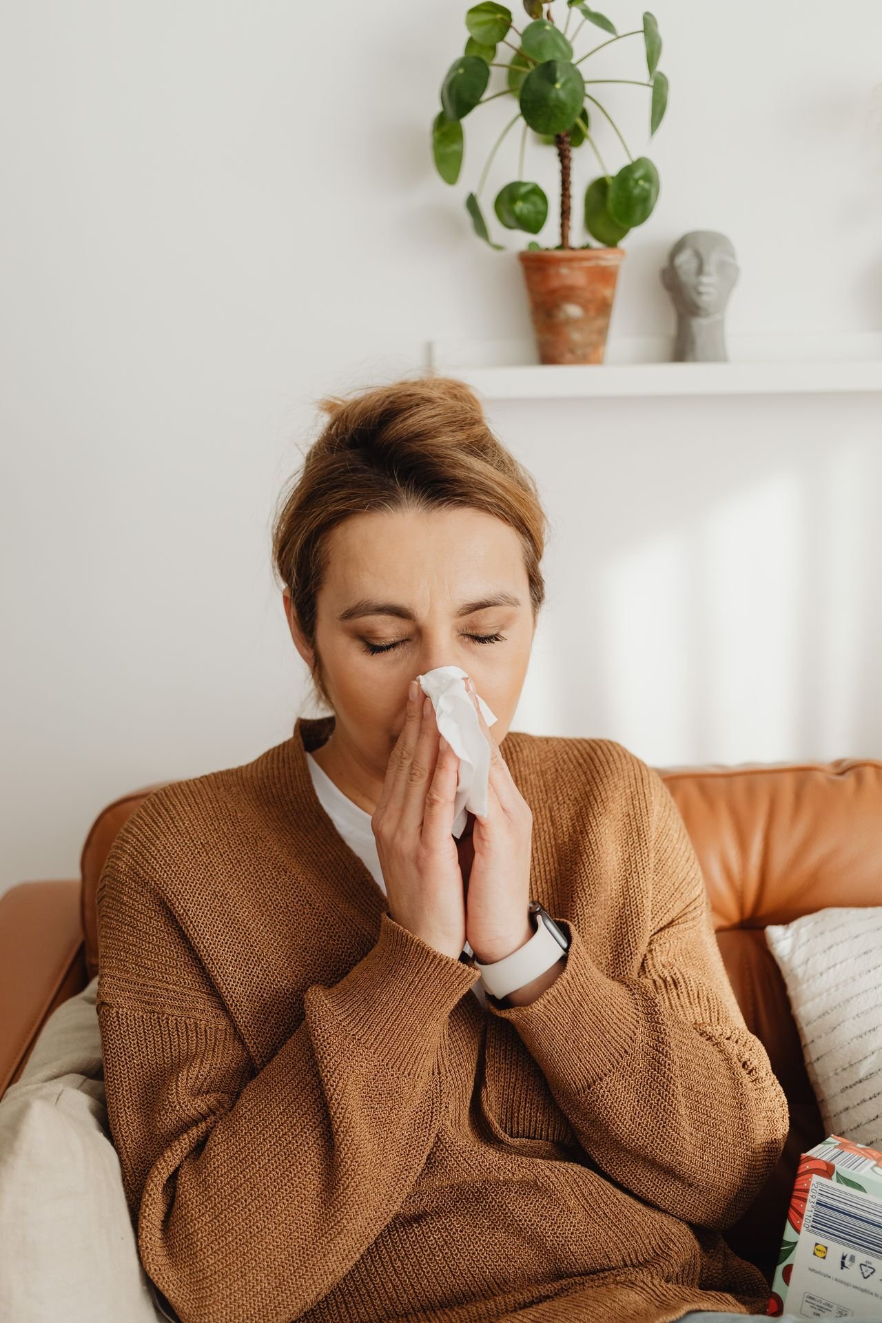 Close-up of a woman blowing her nose while sitting on a sofa