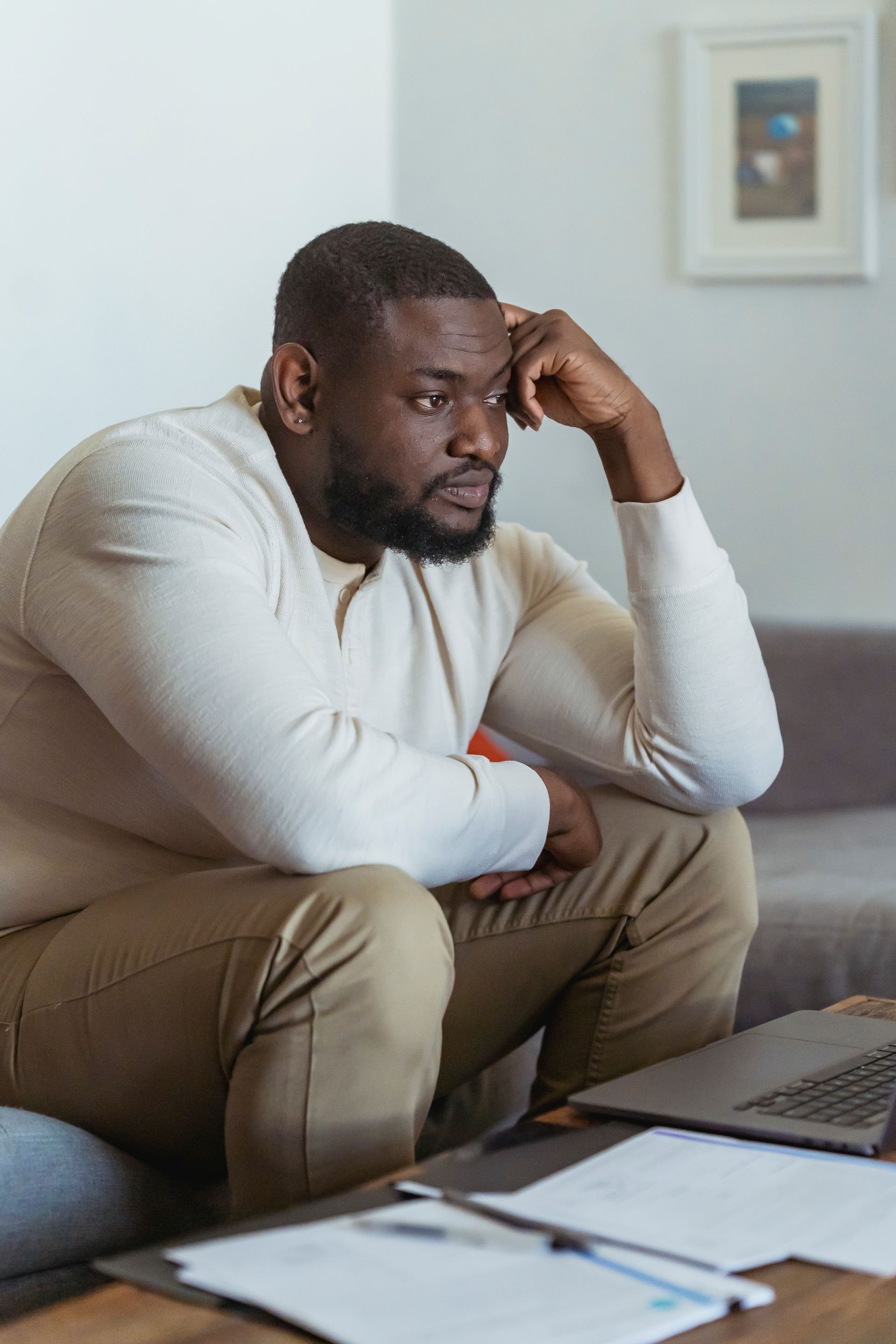Man sitting on a sofa looking pensive with his hand resting on his forehead
