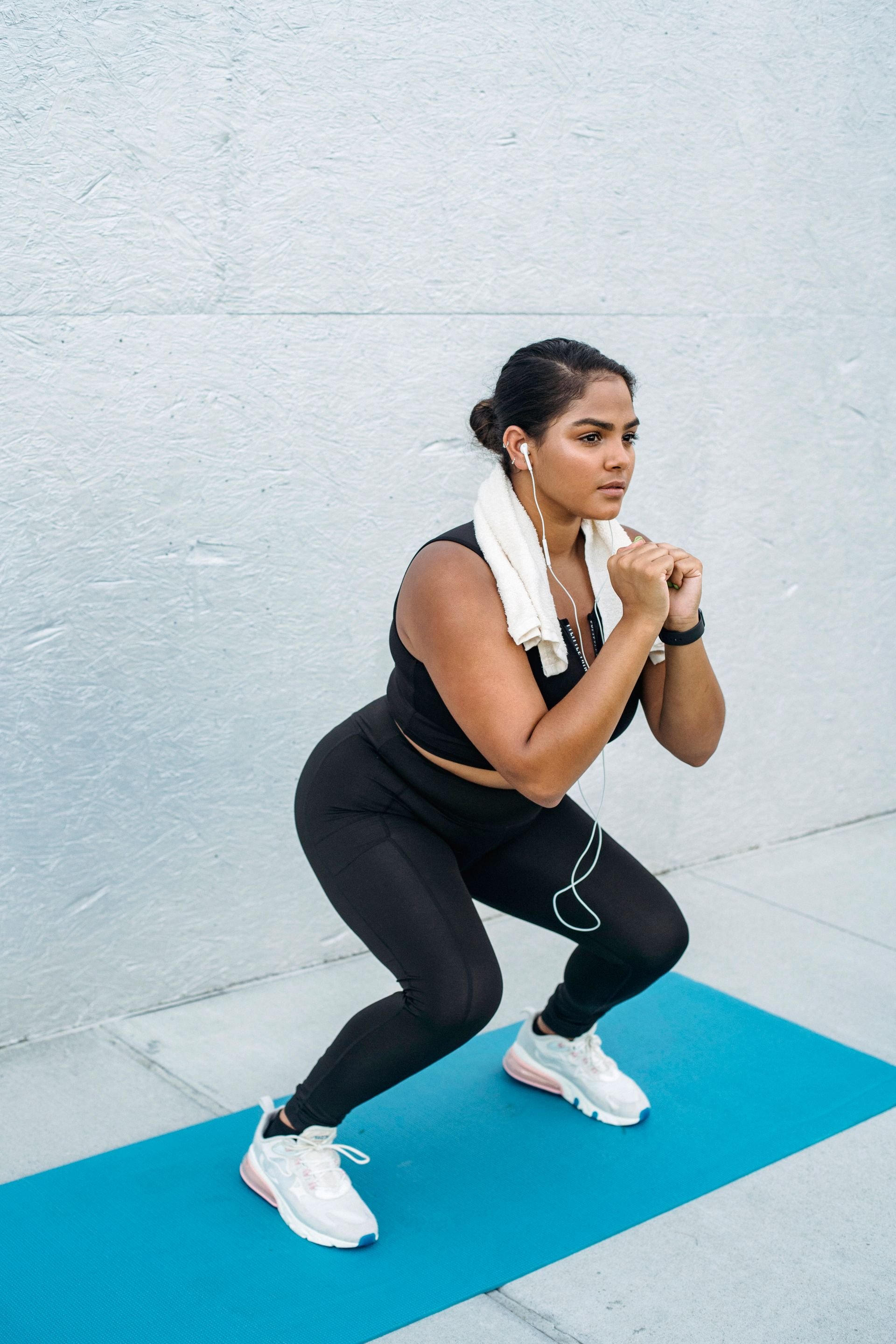 woman crouching mid-exercise with a towel around her neck