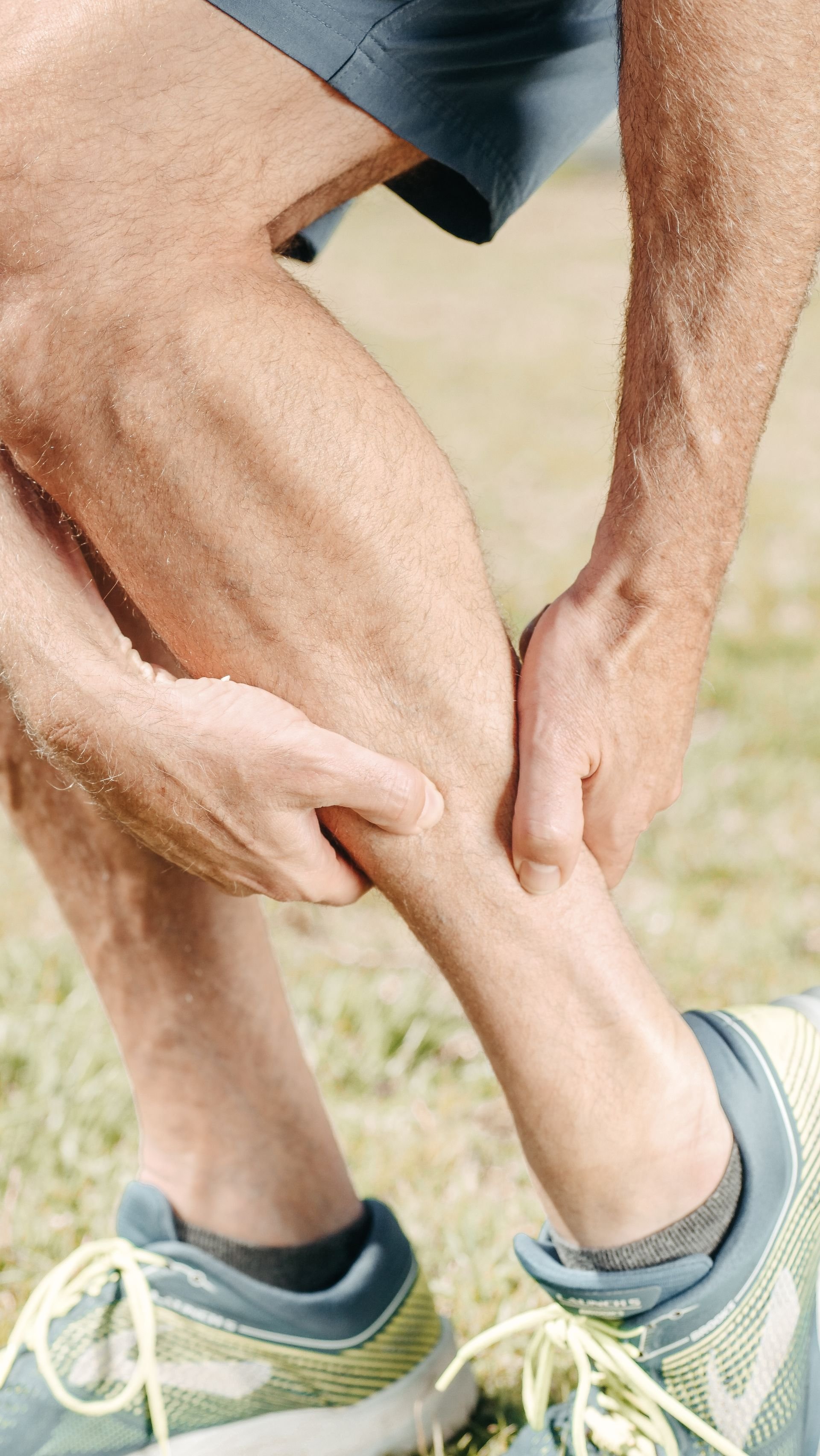Close-up of a man holding his calf in pain outdoors