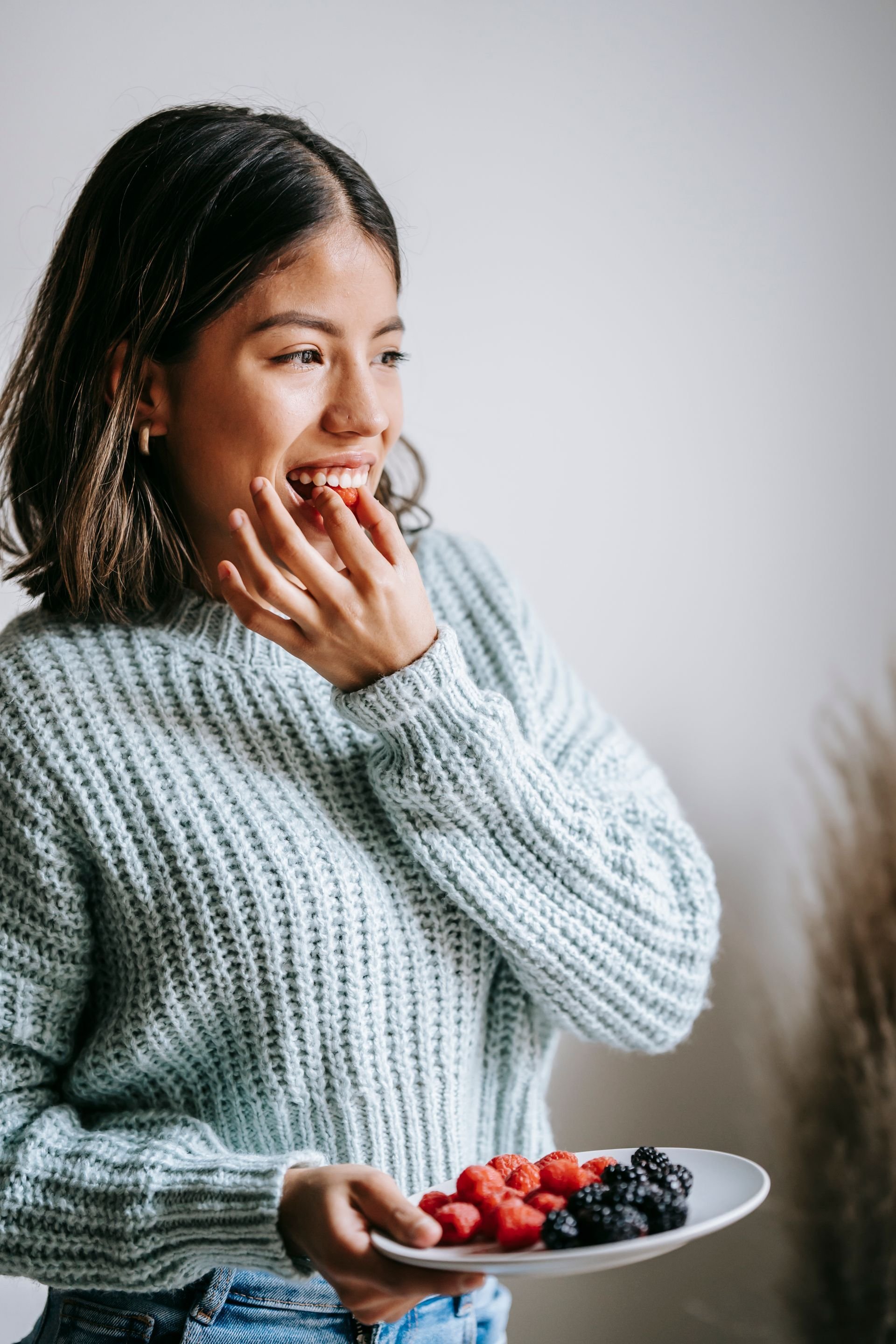 Woman in a chunky knit jumper smiling with her fingers near her mouth