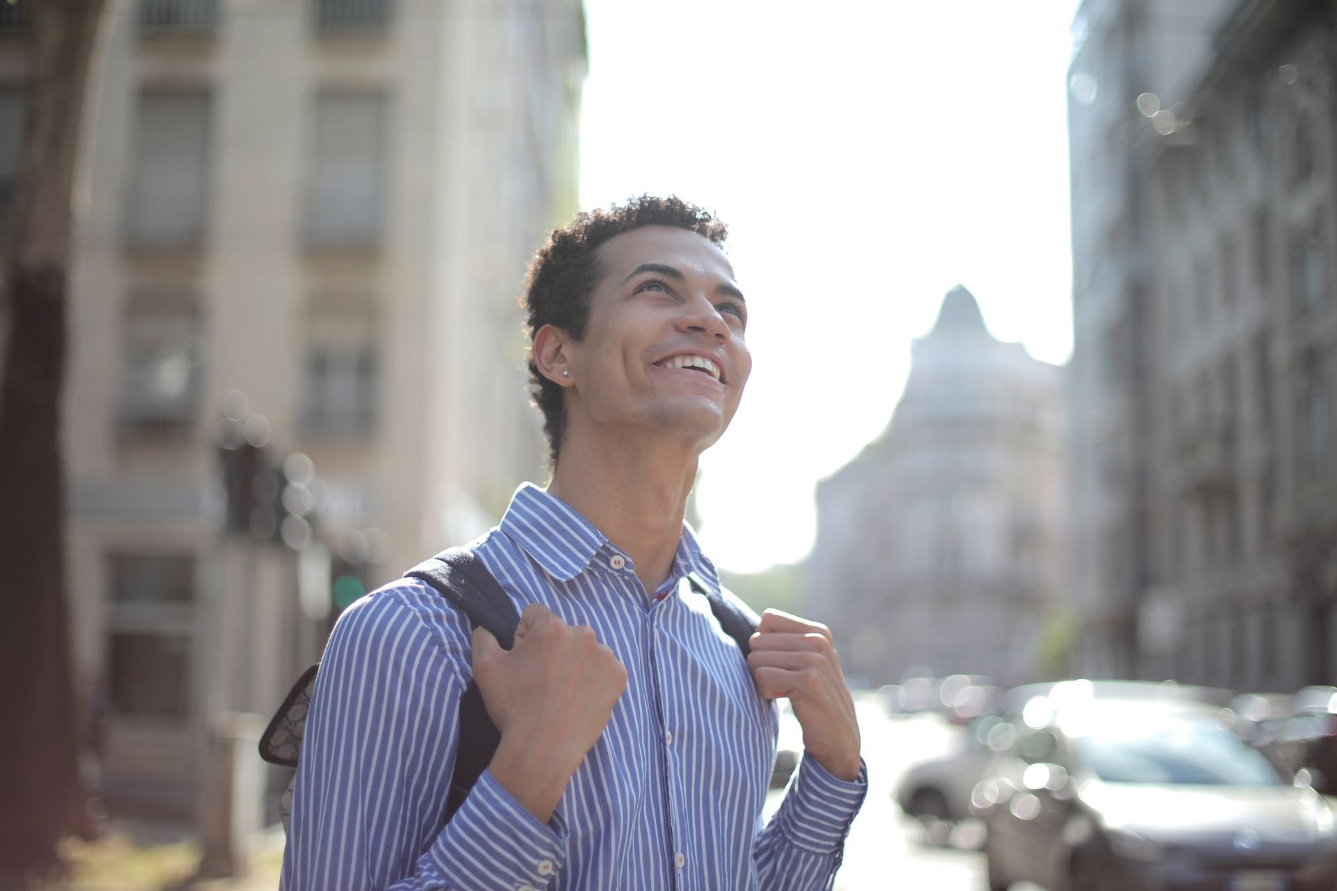 Smiling man with a backpack looking up while walking through a city street
