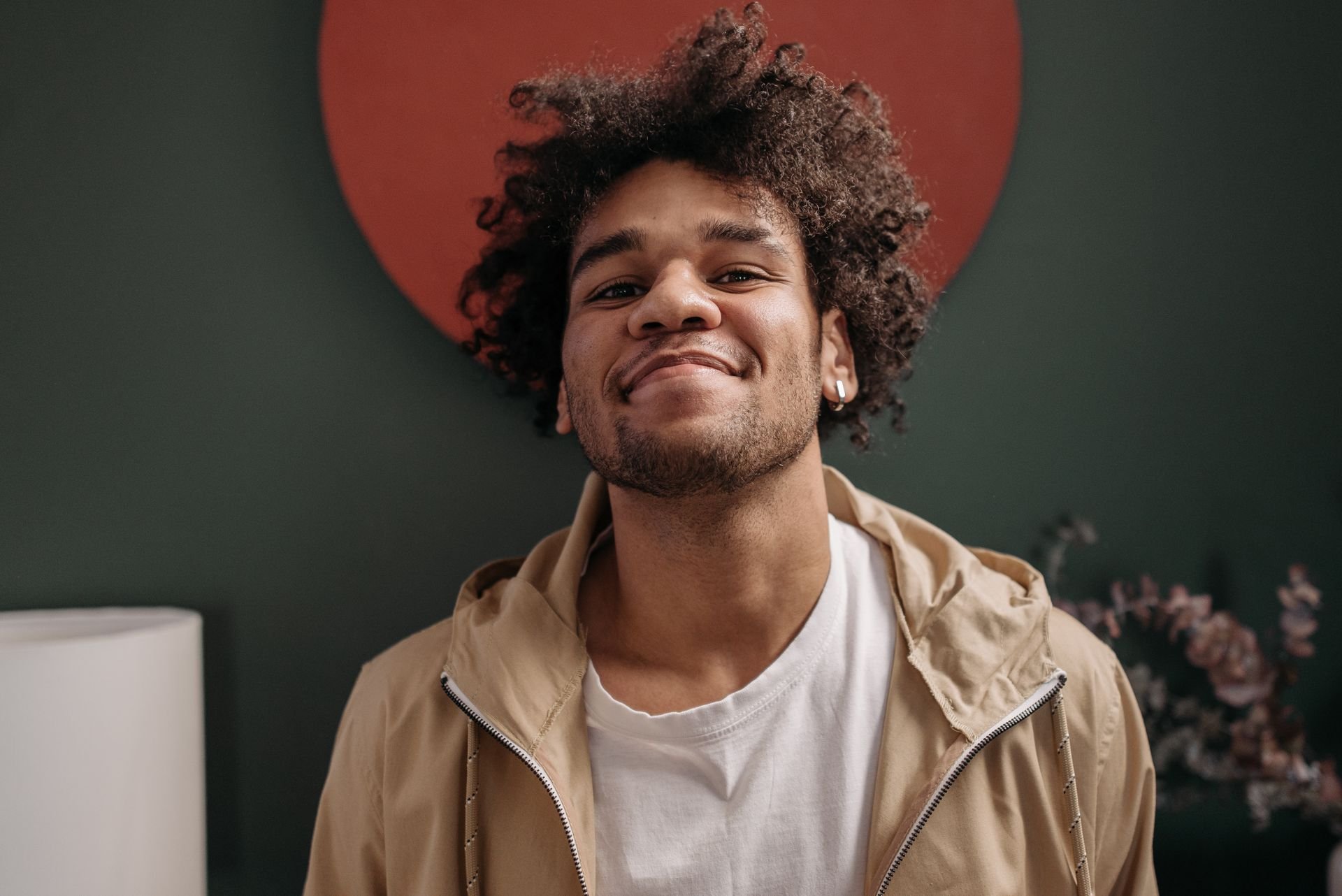 Smiling young man with curly hair against a green wall with a red circular backdrop