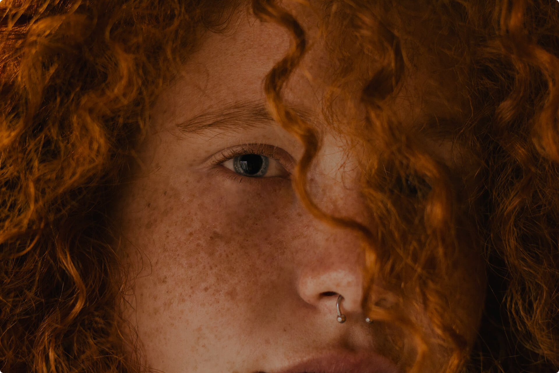 Portrait of a young woman with a nose ring, freckles and red curly hair