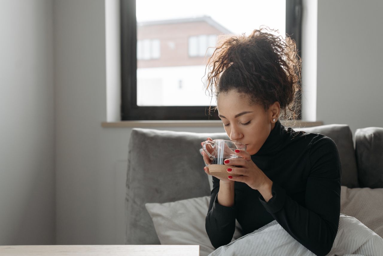 Woman sitting on a sofa at home holding a warm drink with both hands